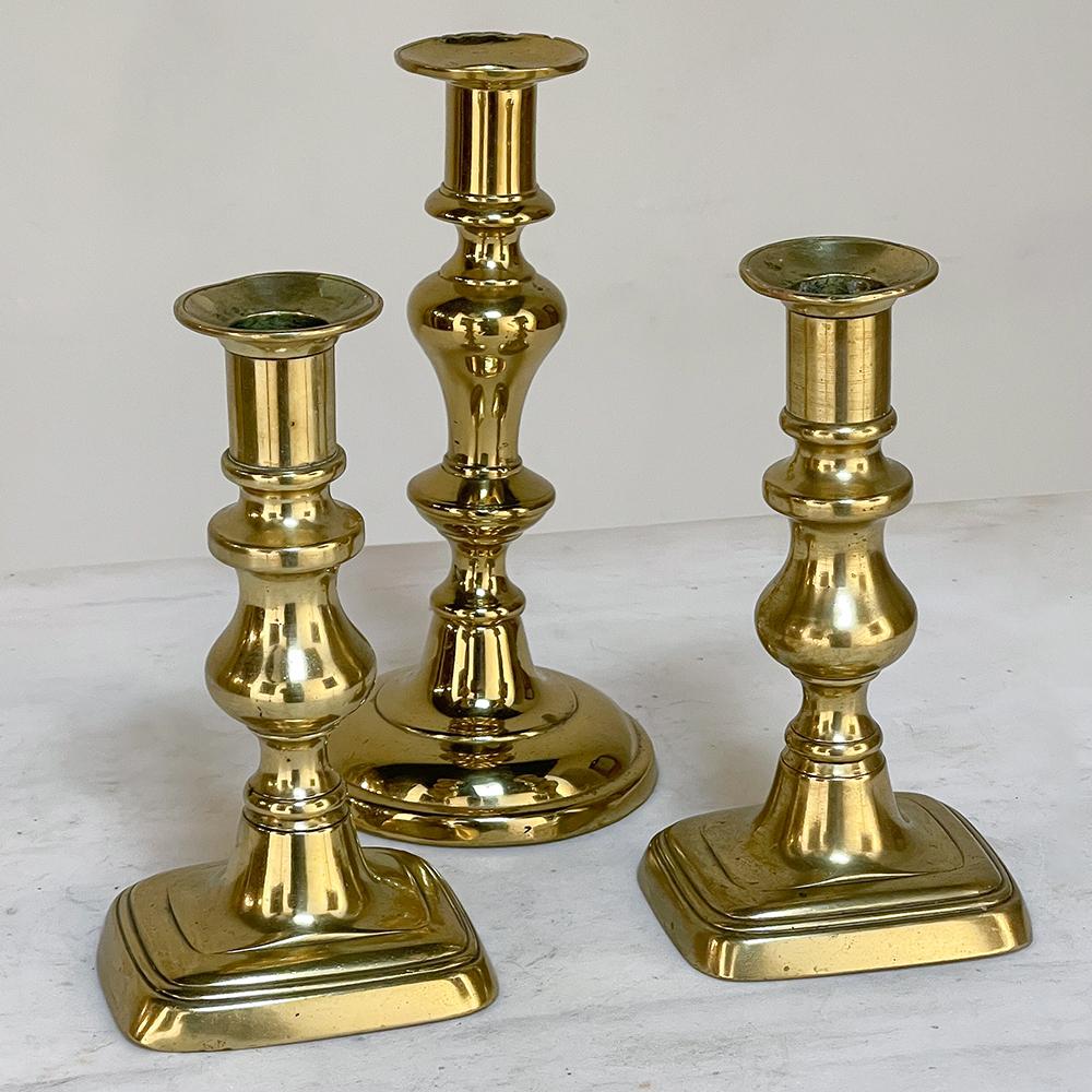 Set of Three 18th Century Hand-Made Brass Candlesticks were designed to be functional yet attractive as they would remain in plain view all day, and only be utilized at night.  Back in the days before electric lighting, candles were worth their
