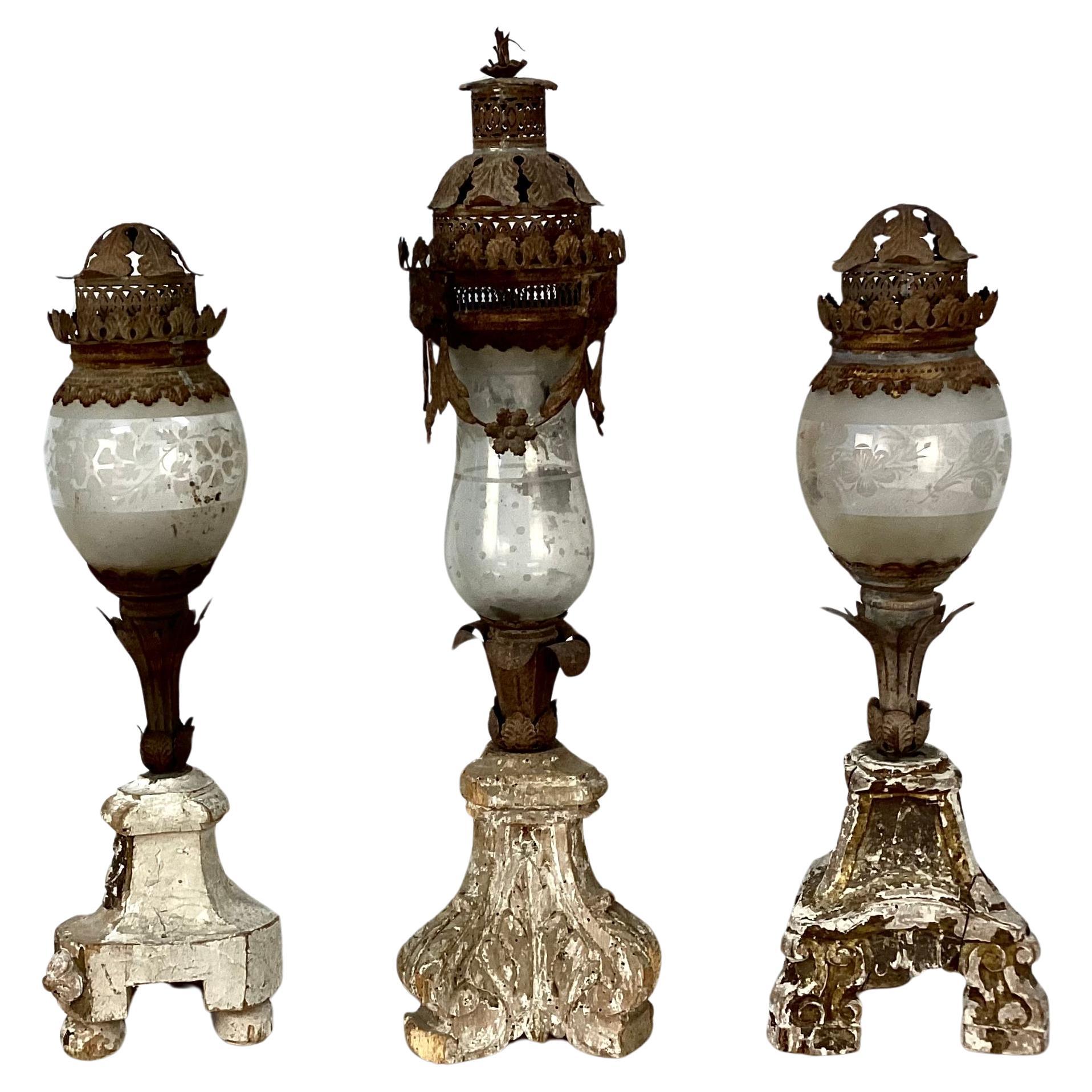 Set of three ornate 18th century giltwood and tole lanterns. Lanterns are of three sizes, each having glass centers with frosted floral etching, ornate tole metal tops and bodies that resemble floral stems, all resting on giltwood ornate bases with