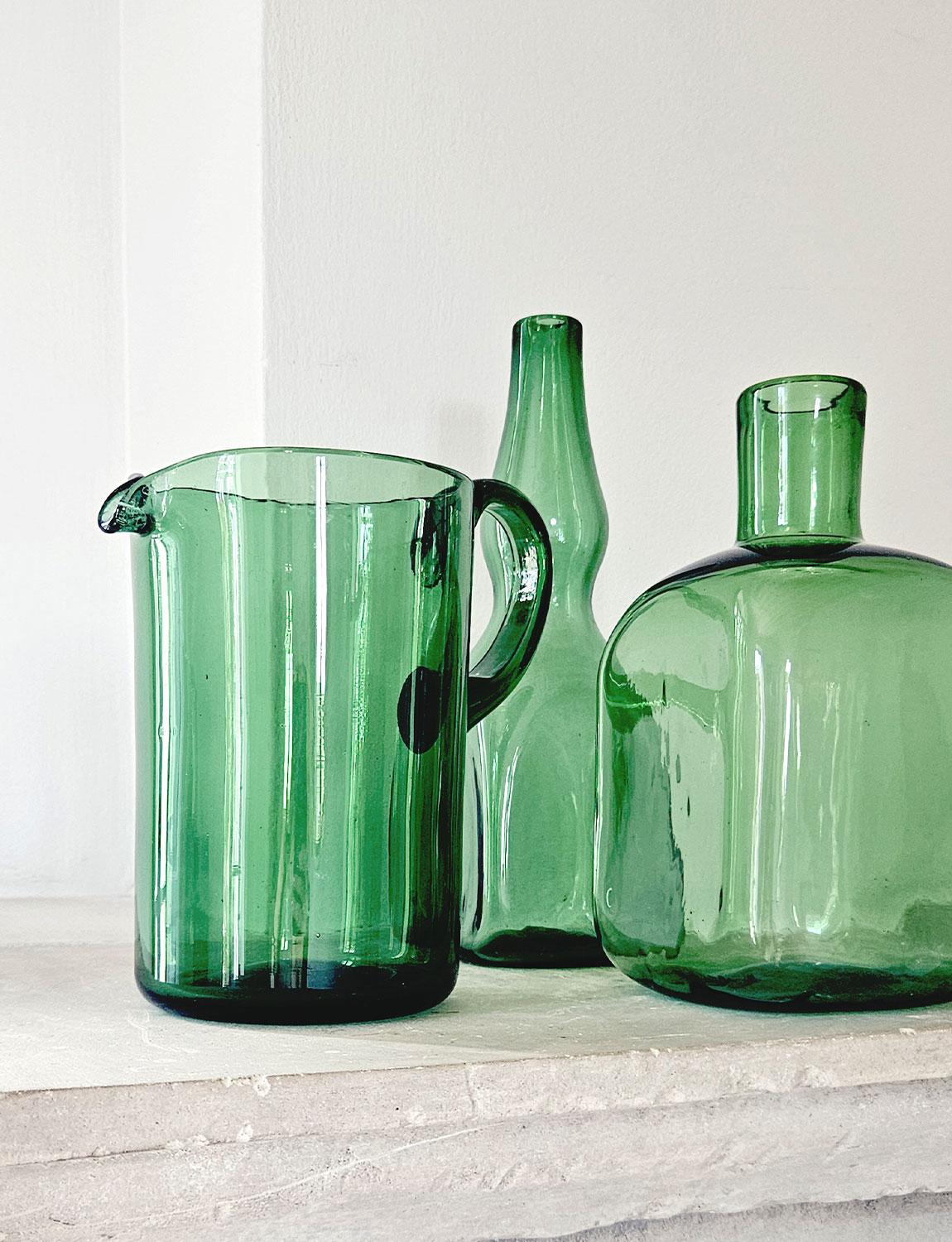 Two 1950s bottles and one jug hand-blown in traditional green glass. Made in Empoli, Tuscany in the 50s, these pieces are perfect for a al fresco summer tables.

Dimensions
Jug: H19cm X W12cm X D12cm
Square Bottle: H22cm X W11cm X D11cm
Second