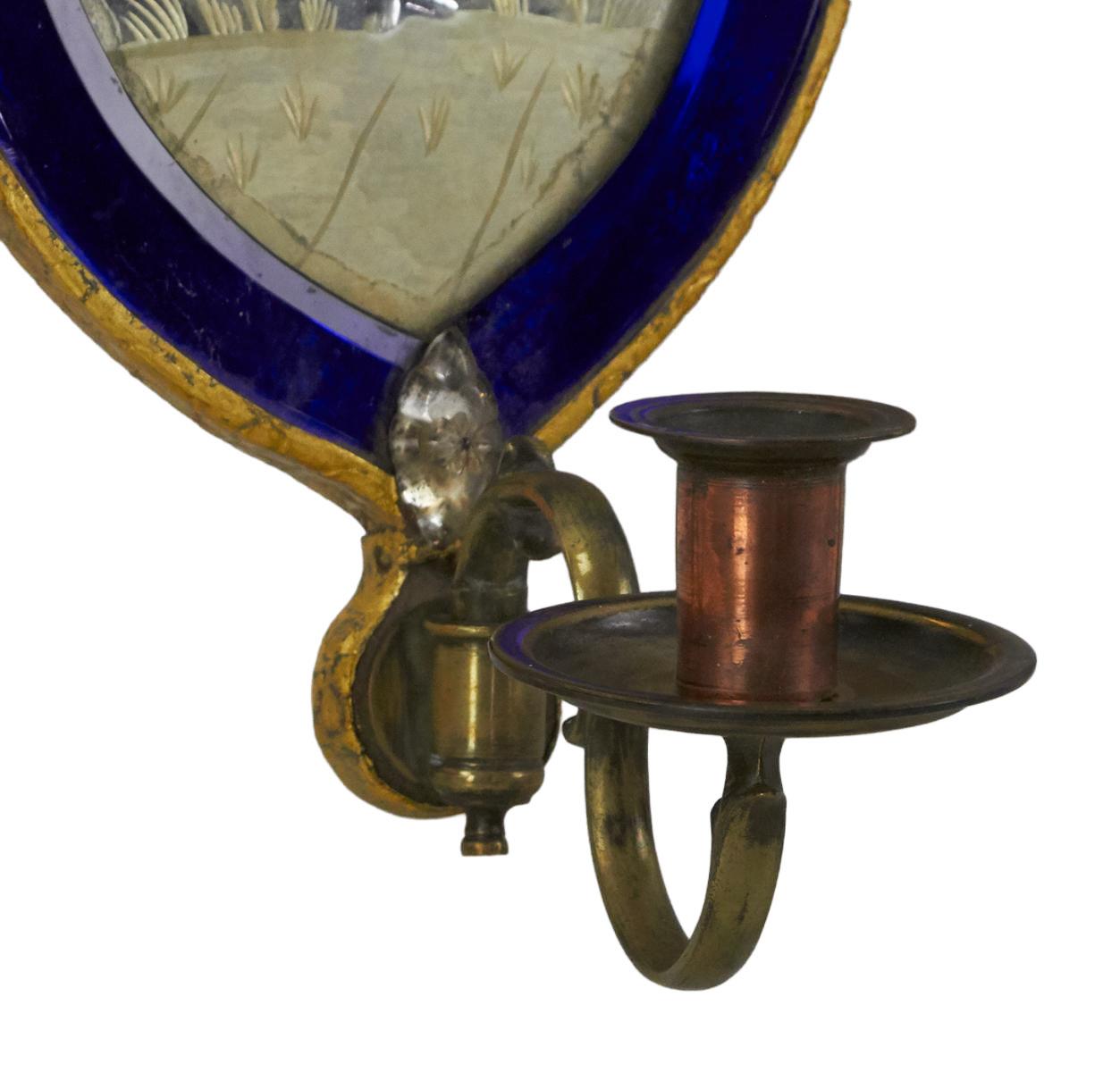 A trio of English Regency cobalt mirrored sconces, adorned with intricate engravings on their mirror faces, exhibit a captivating aesthetic. Two of the mirrors bear subtle hairline cracks, imperceptible upon initial inspection, while the outer edges