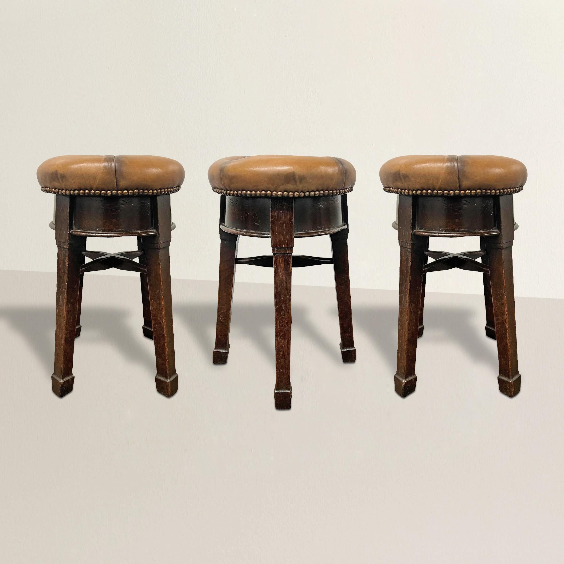 These three 19th-century English Arts & Crafts pub stools with nailhead trim are a stunning blend of functionality and craftsmanship. Influenced by the Arts & Crafts movement, each stool features a distinct design characterized by clean lines,