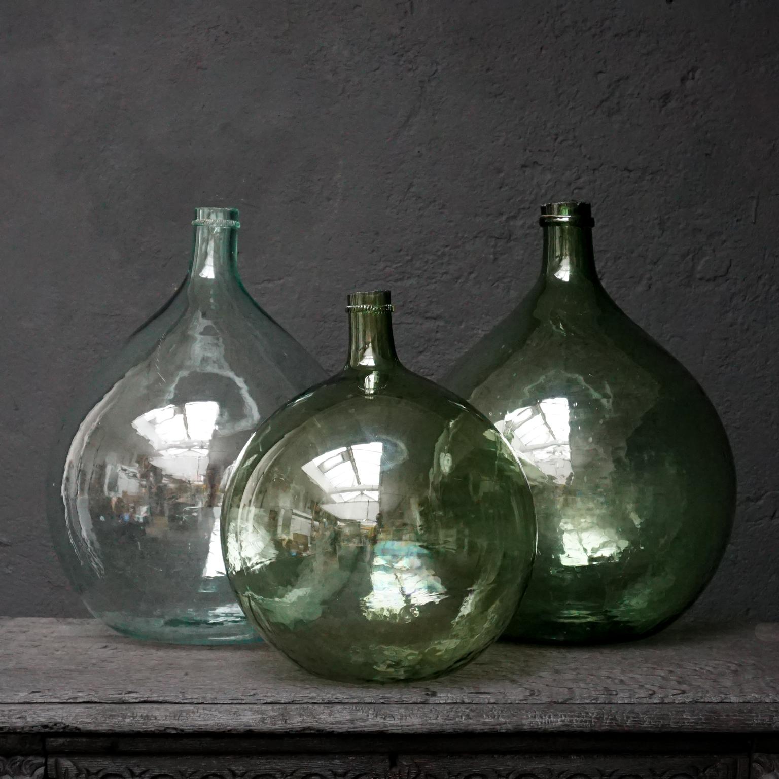 Wonderful set of three French different shades of green, blown wine bottles, also known as Dame Jeanne, Demijohn, Carboy or Bonbonne bottle

All three are hand blown in a globular form mould with hand added bottlenecks.
The two larger ones are
