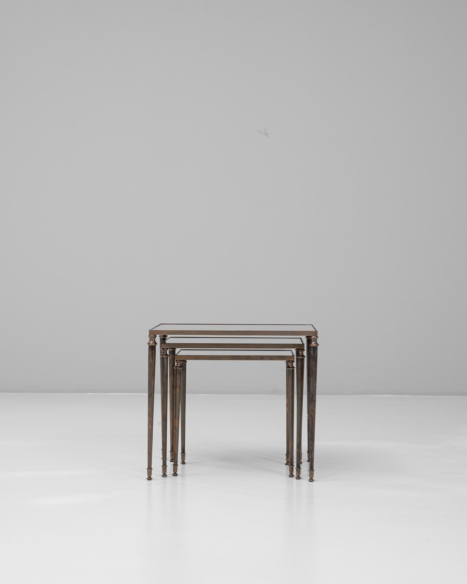 This elegant set of three 20th Century French nesting tables showcases a refined balance of craftsmanship and versatility. Each table features a brass frame with slender, tapered legs capped in delicate feet, lending a neoclassical air to the