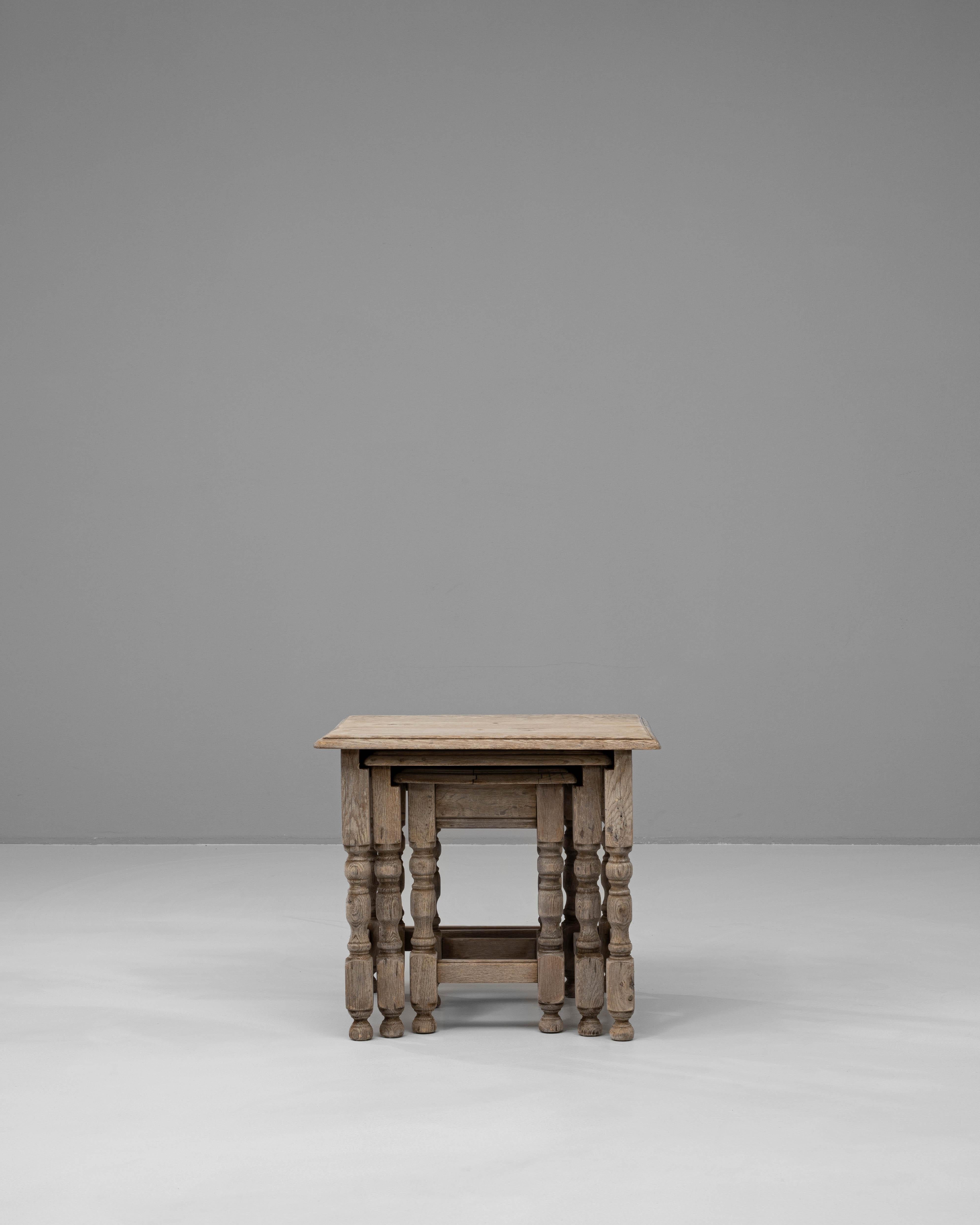 These 20th-century French oak nesting tables showcase timeless craftsmanship and practicality. The set of three tables, graduated in size, features turned legs and cross-stretchers, highlighting the elegance of traditional woodworking. The oak