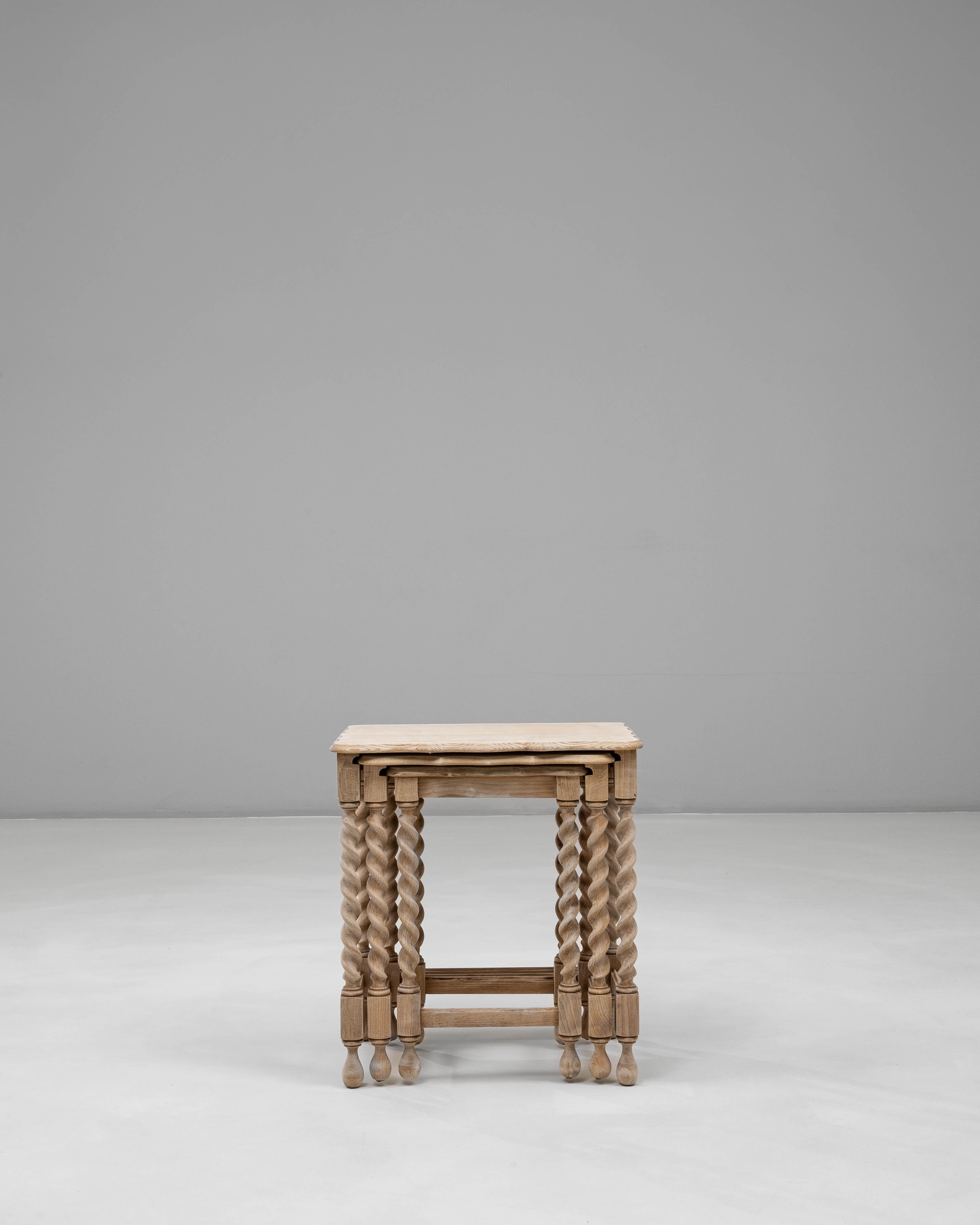This set of three 20th Century French oak nesting tables showcases elegant craftsmanship with beautifully carved barley twist legs and a warm, lightly washed finish. Each table features a simple rectangular top with subtle edge detailing, allowing