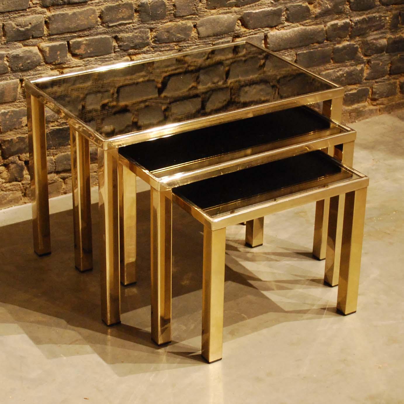 This beautiful set of three nesting tables was made in the early 1980s by Belgian Belgo Chrom. 
The tables have a metal frame that was gold plated with a thin layer of 23-carat gold. The tables feature a smokey glass mirror inlaid top. The legs are