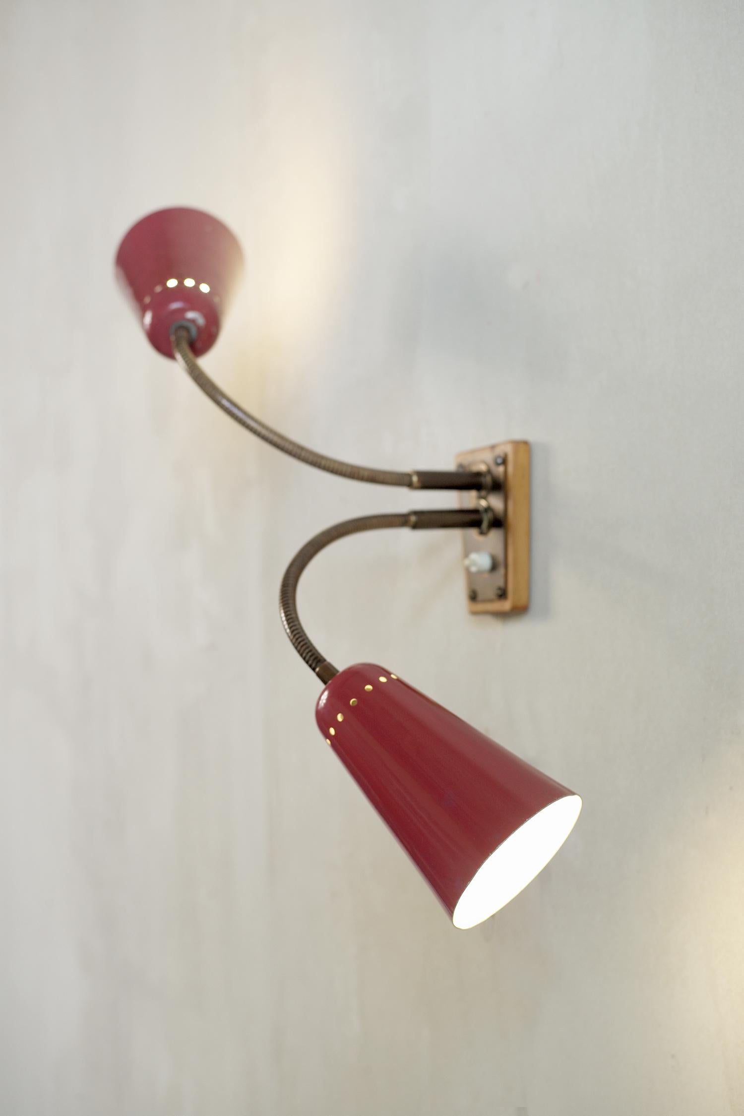 Set of three wall lights in gilt brass and perforated and carmine lacquered metal, Italy 1950. One wall light is equipped with a reflector on a flexible tube, the second has two arms on a flexible tube and the third has two adjustable reflectors and