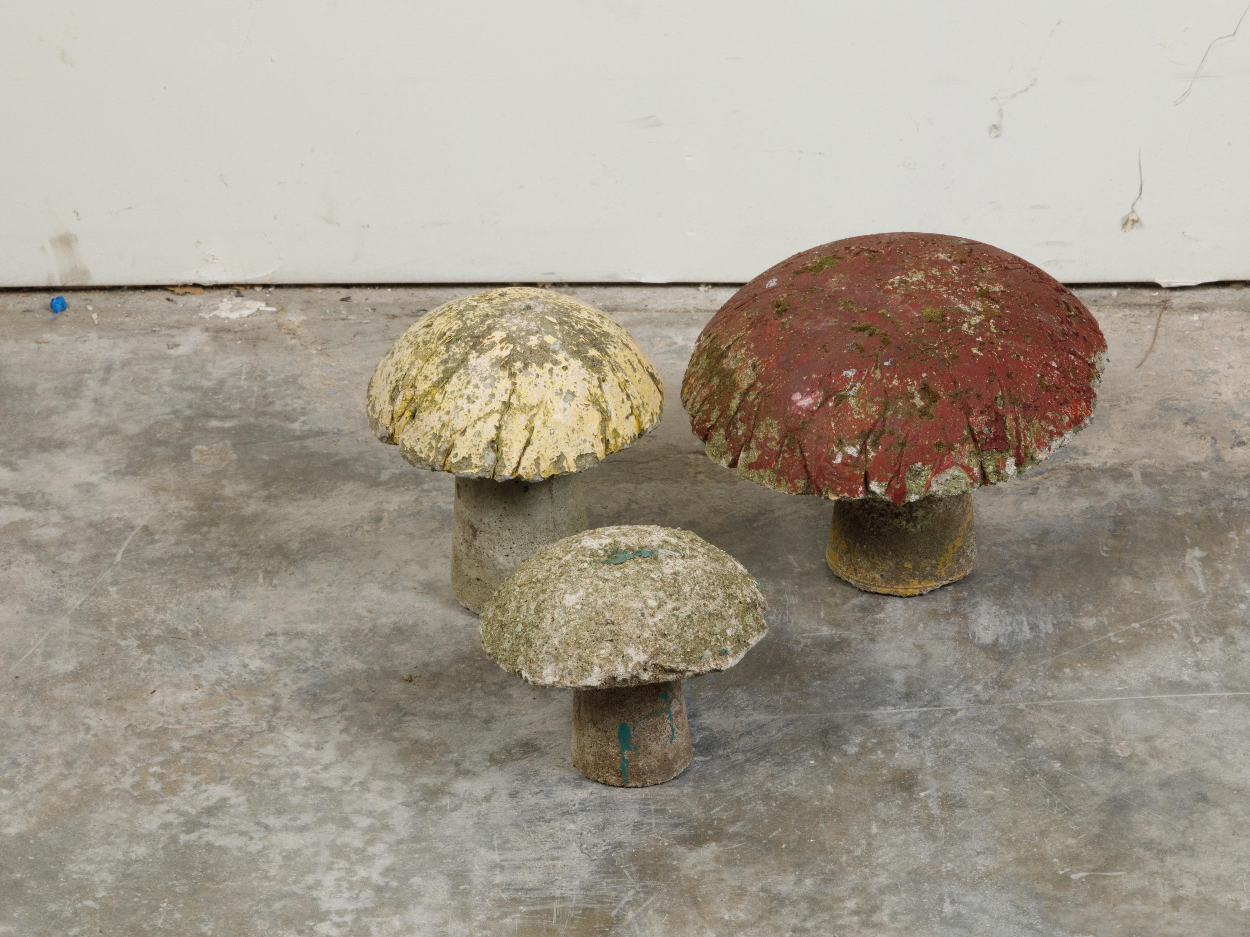 A set of three vintage American concrete mushrooms from the mid-20th century, with nicely worn patina. Made in the USA during the mid-century period, this set of three concrete mushrooms boasts a nicely weathered appearance, with yellow, red and