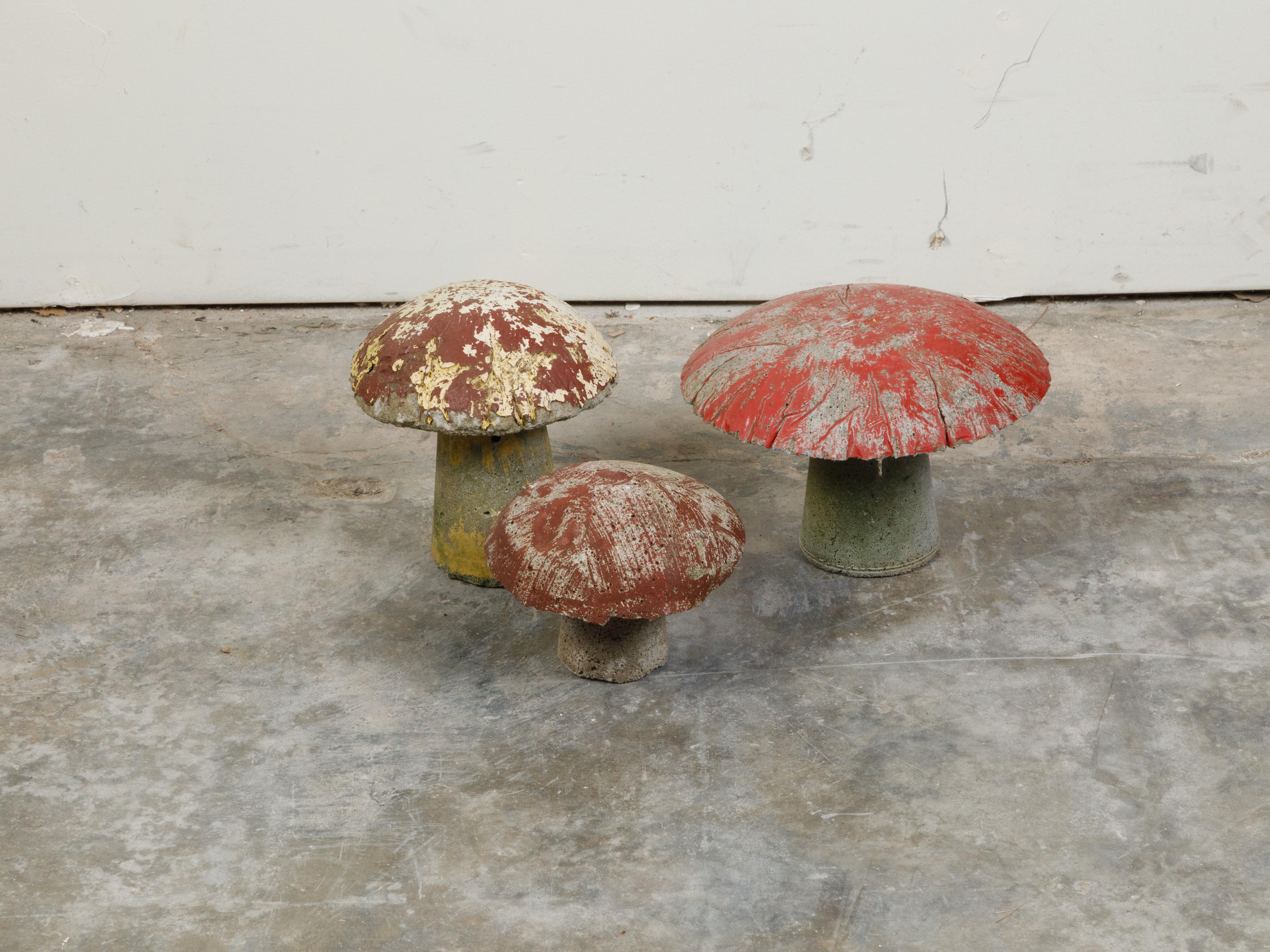 A set of three vintage American concrete mushrooms from the mid 20th century, with nicely worn patina. Made in the USA during the midcentury period, this set of three concrete mushrooms boasts a nicely weathered appearance with red, yellow and green