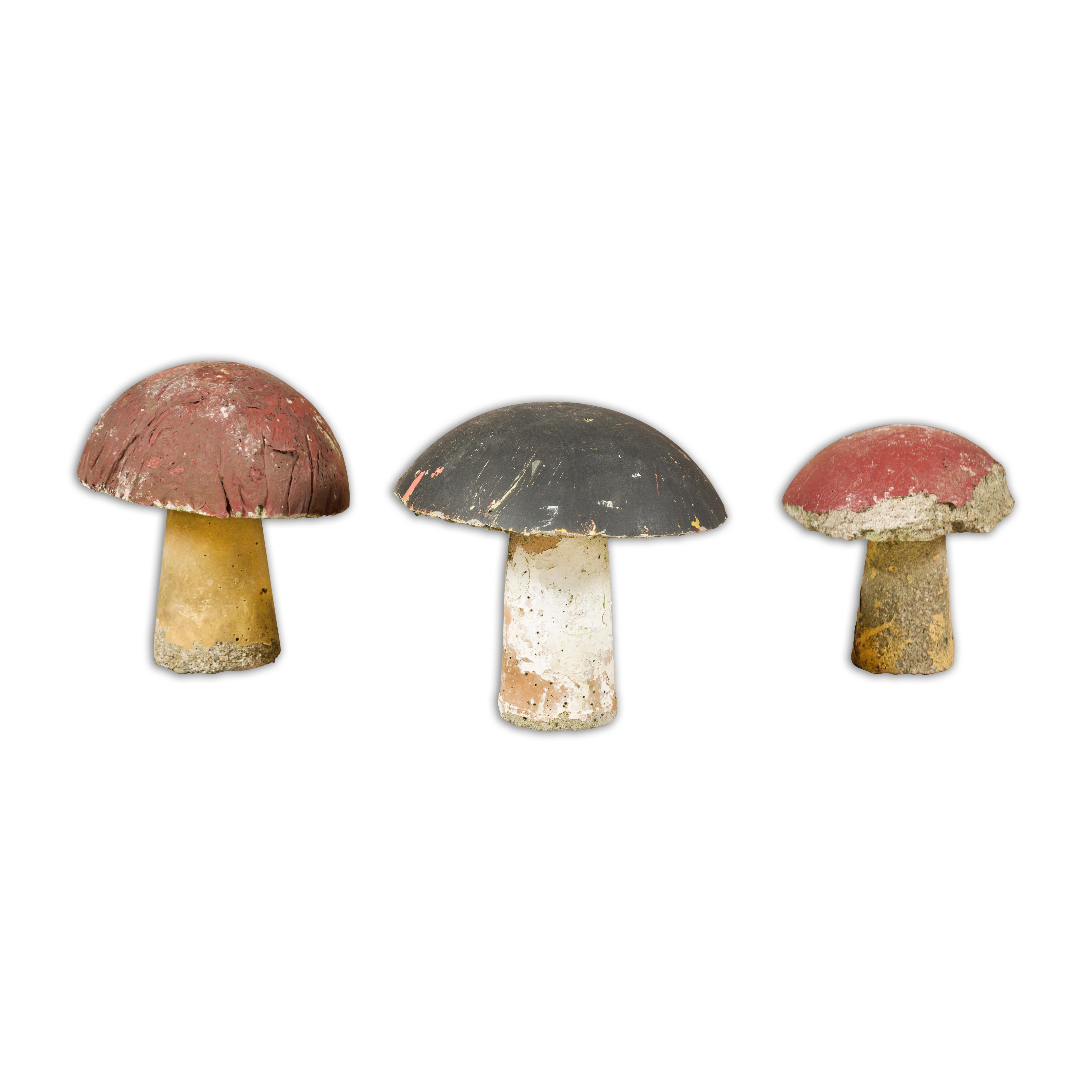 A set of three American Midcentury painted concrete mushroom garden ornaments with red and black tops and nicely weathered appearance. Envelop your garden in a veil of enchantment with this set of three American Midcentury painted concrete mushroom