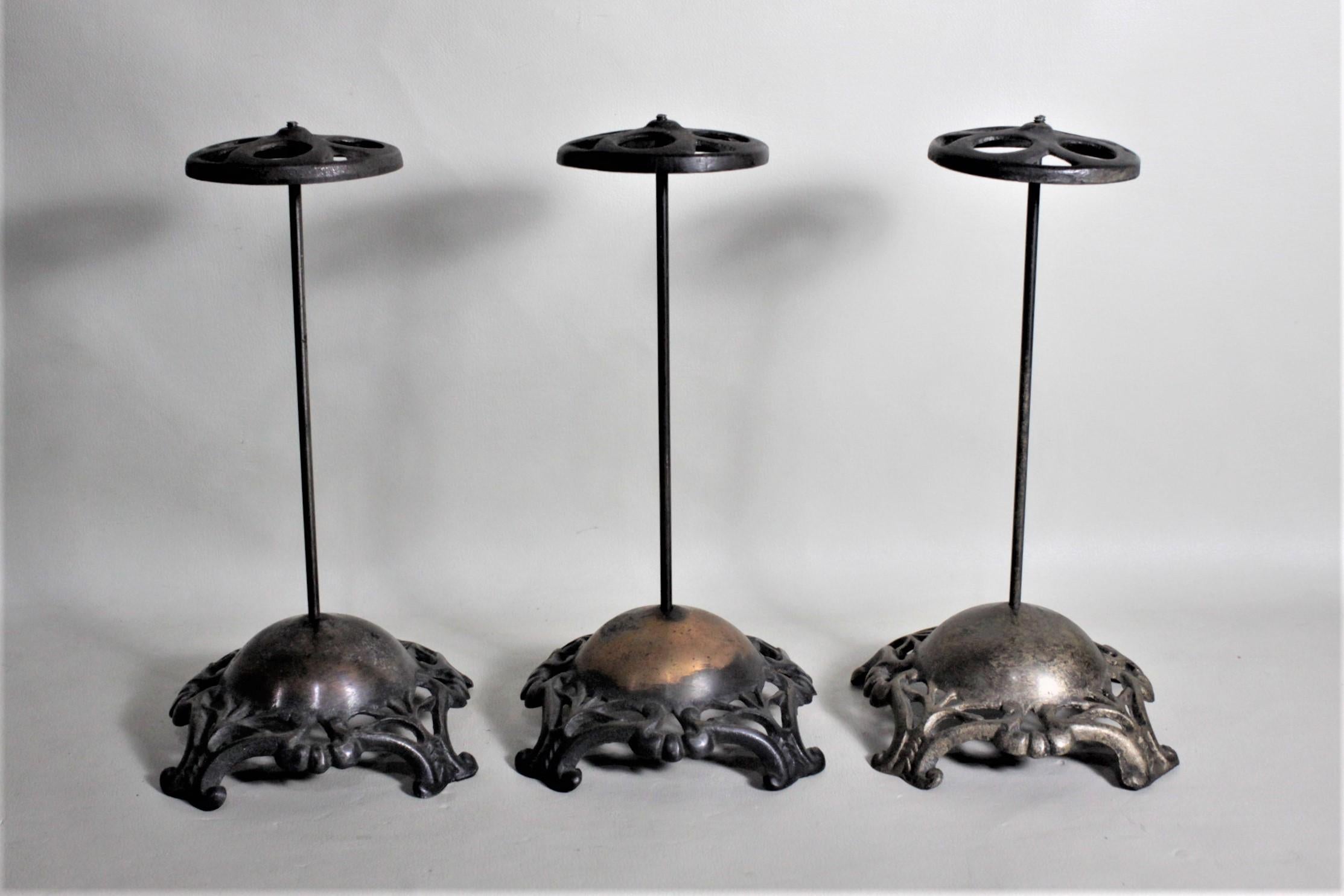 This set of three cast metal hat stands have no maker's marks but are presumed to have been made in the United States in circa 1880 in the period Victorian style. The stands have cast bases with a bronze patina and cast pierced tops. The stands are