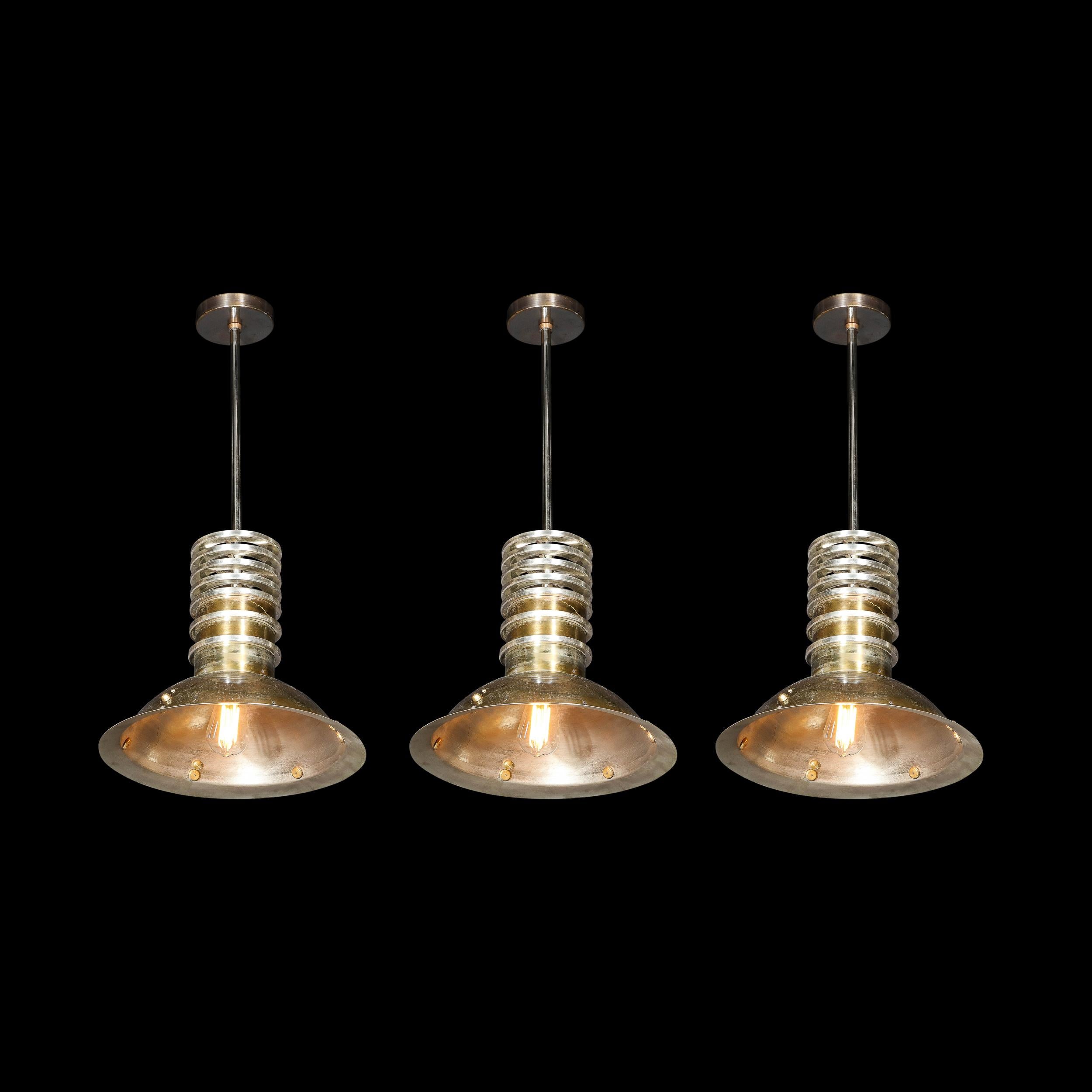 This very sophisticated set of three Art Deco industrial pendants were realized in France, cirac 1940. They feature domed concave bodies in antiqued bronze that affix to a cylindrical body in the same material circumscribed by three evenly spaced