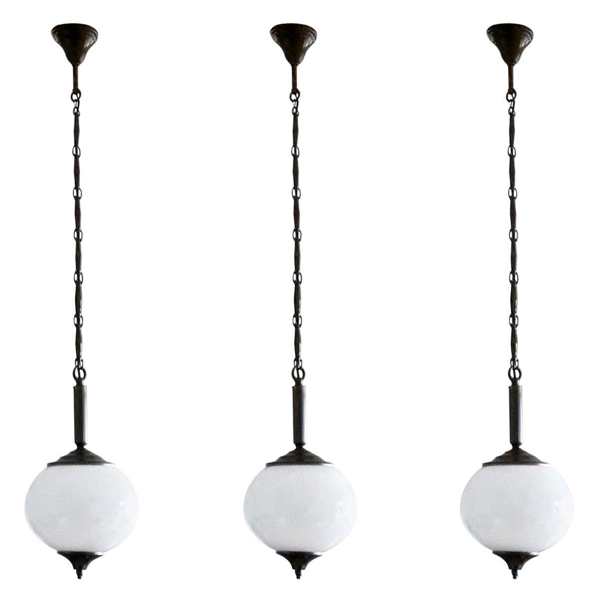 A set of three Italian hand blown opaline globe pendants, burnished brass mounts, chain and canopy, 1940-1949.
European wiring with a single brass and porcelain Edison E-27 light socket for large sized bulb (each pendant).
Measures: Height 41 in /