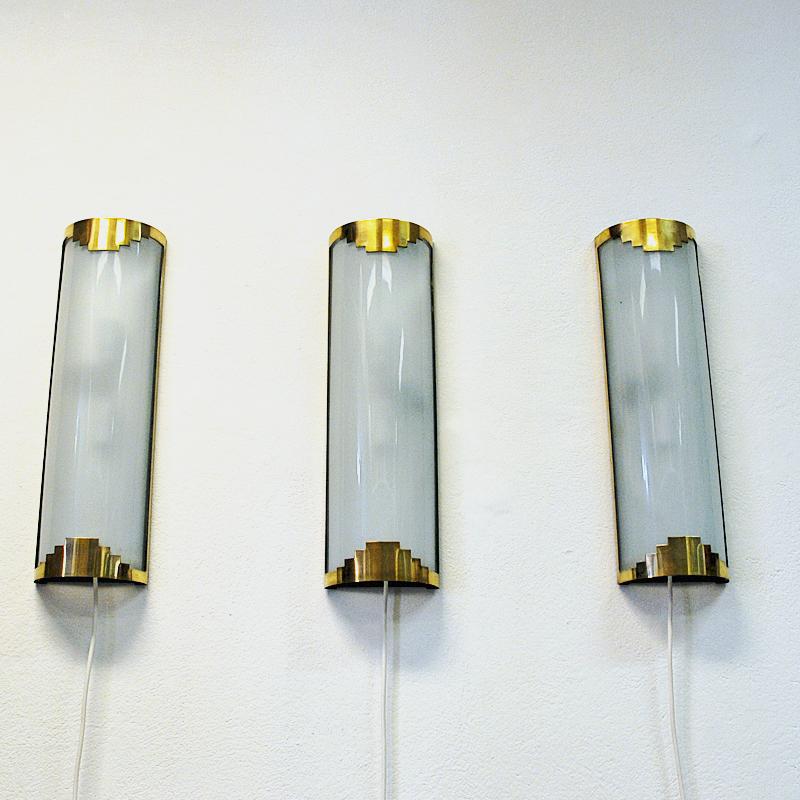 Lovely triple set of Art Deco rectangular wall lamps of brass and frosted glass on a metal base to be attached to the wall. Rounded shape and design. Gives a lovely and pleasant calming light in every room. Lovely as a set of three together or
