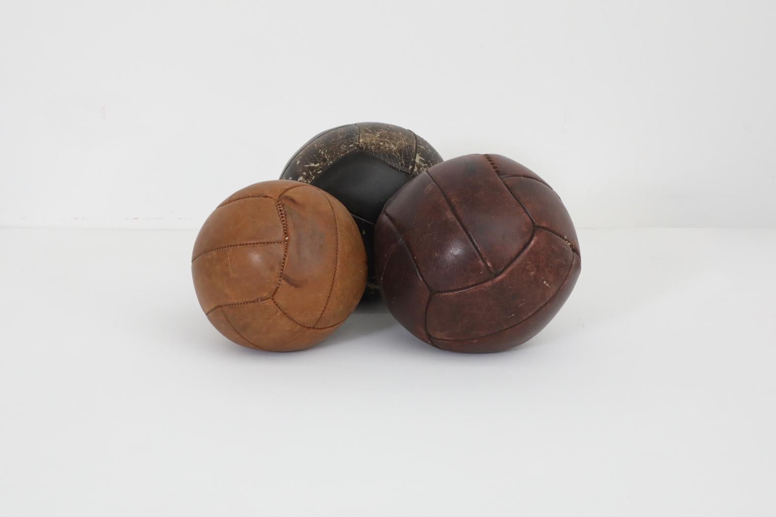 Juego de tres balones medicinales gimnásticos de cuero de los años 50 en tonos de cuero surtidos. Cada balón tiene cuero original con desgaste y pátina visibles, y reparaciones hechas en las costuras. Los diámetros y pesos aproximados son los