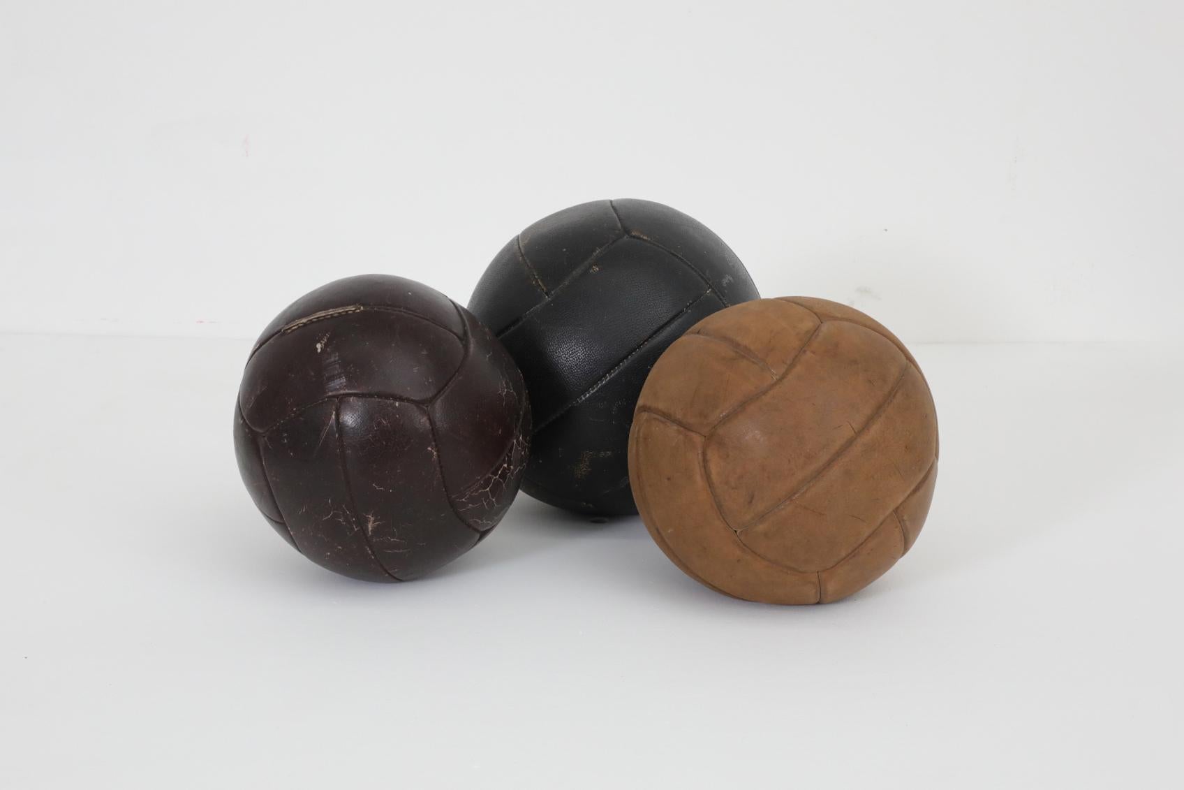 Set of three 1950's leather gymnastic medicine balls in assorted leather tones. Each ball has original leather with visible wear and patina, and repairs made to the stitching. Approximate diameters and weights are as follows: 8.5