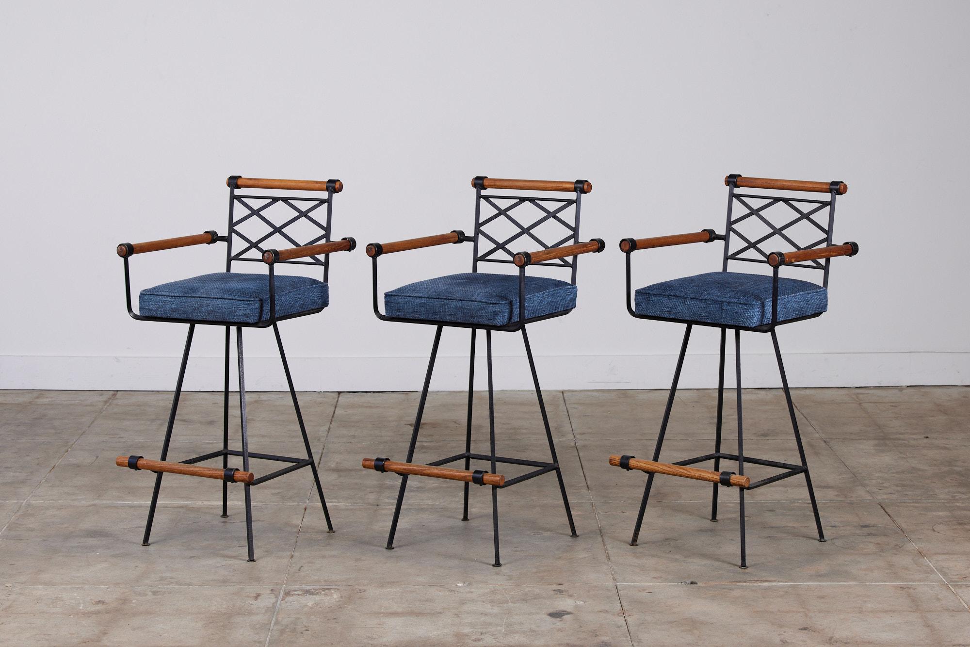 A set of three bar stools for Inca Products, USA, c.1960s in the style of Cleo Baldon. The chairs feature a wrought iron frame with lattice detailed seat backs. Each stool has four long delicate wrought iron legs and a swivel chair. The seats are