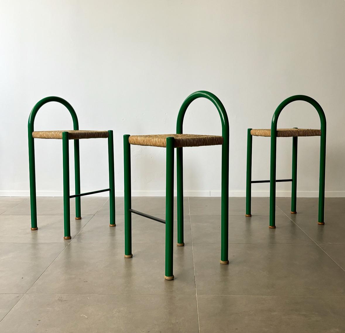 Questo set di tre sgabelli da bar, proveniente dall'Italia degli anni '70, incarna la miscela di modernismo elegante e materiali naturali dell'epoca. Realizzato in robusto metallo verde, ogni sgabello vanta linee pulite e minimaliste che catturano