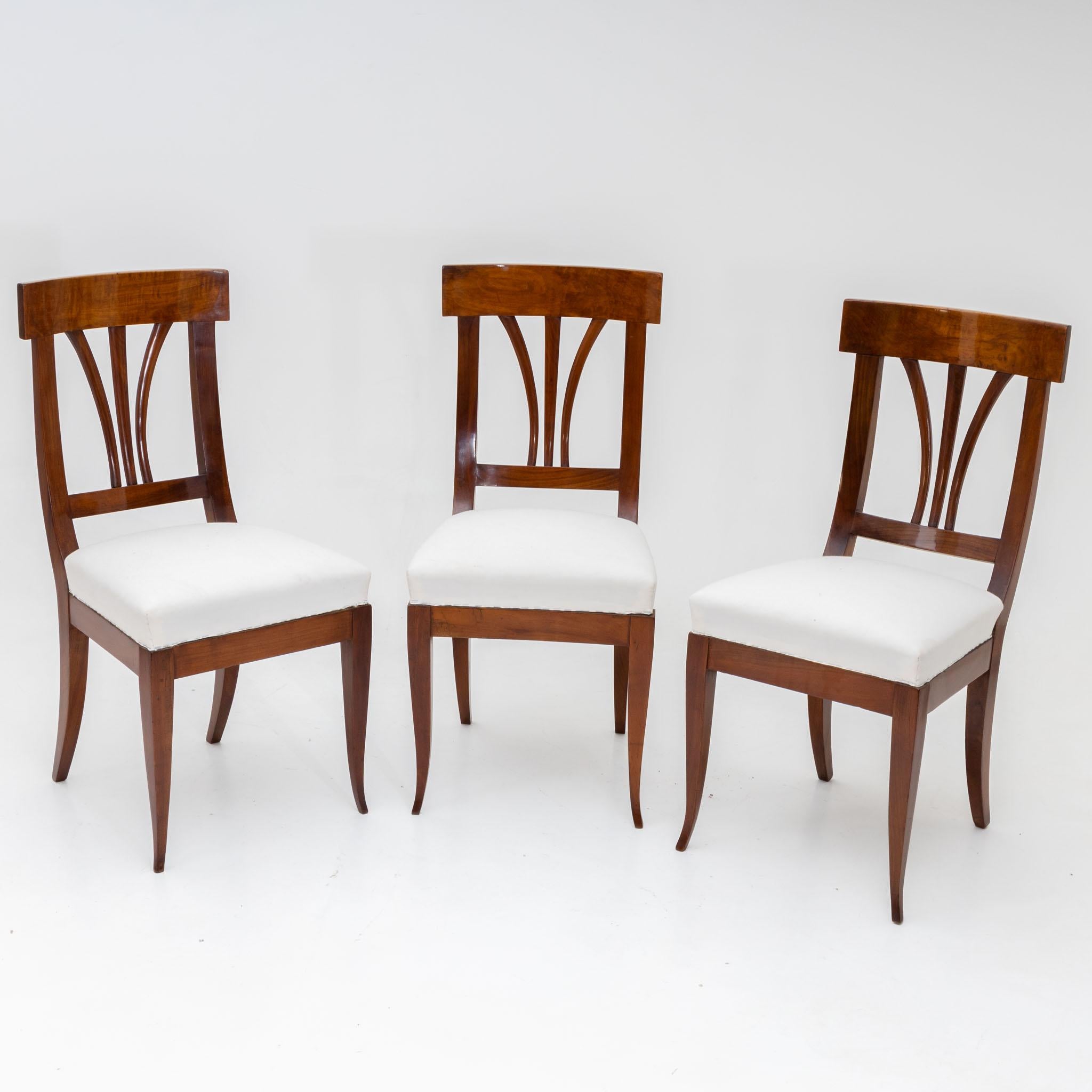 Set of three Biedermeier chairs in walnut with white upholstered seats and backs with three struts. The chairs stand on flared legs and have been newly upholstered and hand polished.