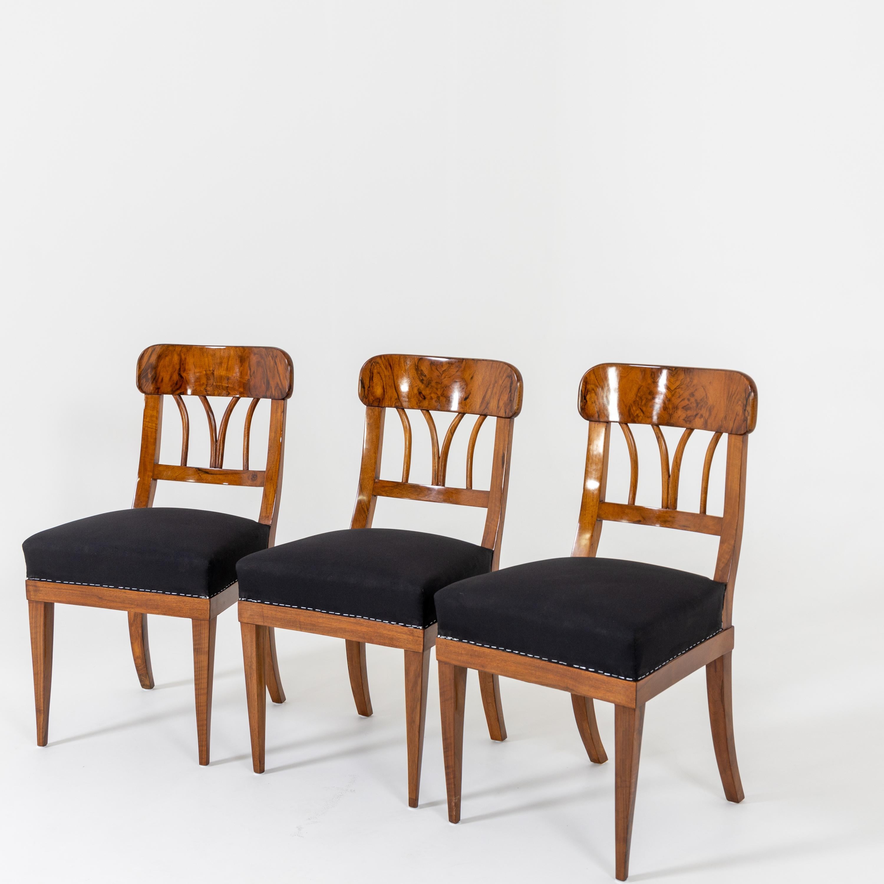 Three Biedermeier chairs in solid and veneered walnut. The chairs stand on square tapered legs and have straight frames and openwork backs with rounded top rails. The chairs were upholstered with a black base fabric.
 
