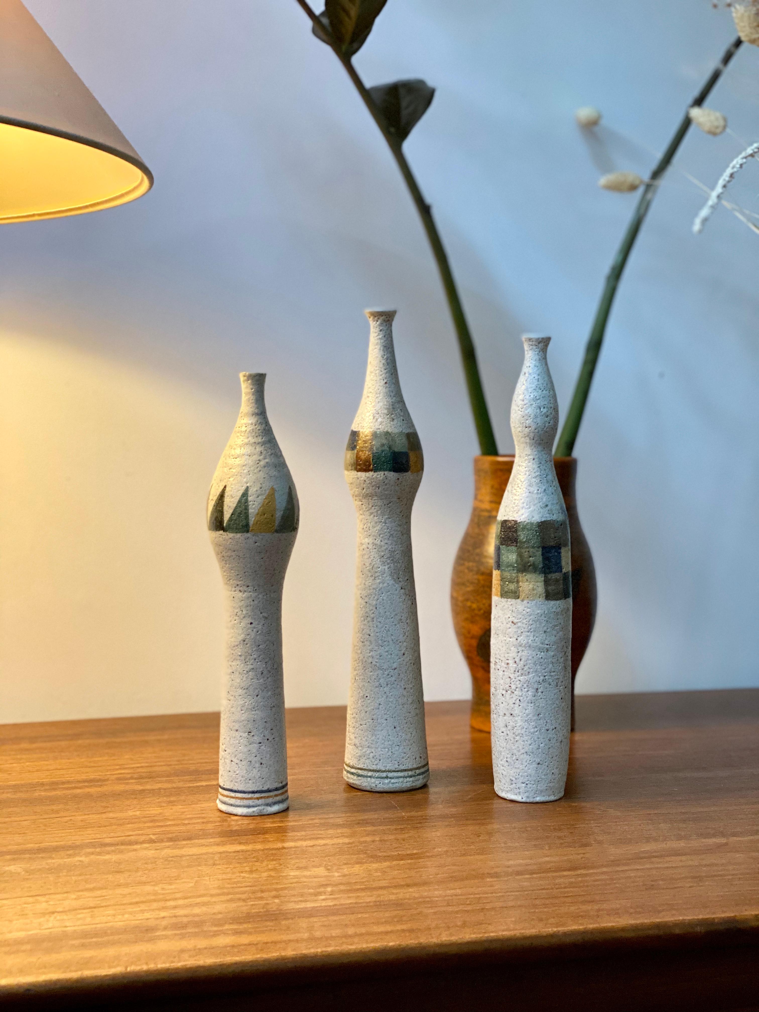 Set of three bottle-shaped single-flower vases by Bruno Gambone (circa 1990s). All three are glazed stoneware pieces with modern, multi-coloured geometric motif. The middle-sized vase has blue colouring which extends beyond one of the geometric
