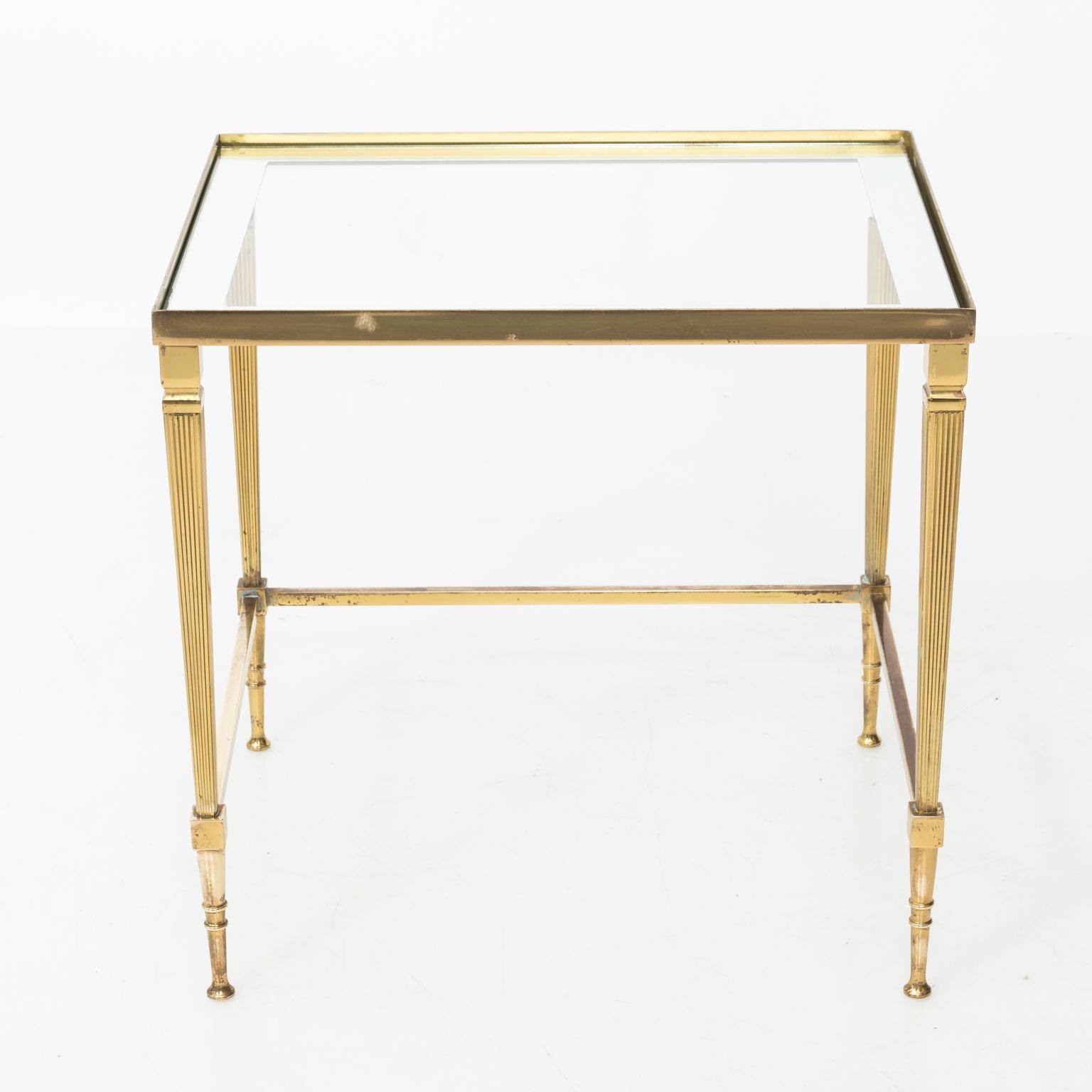 Set of three brass nesting tables with fitted glass tops that have mirrored borders surrounding glass. Dimensions listed are for the largest table, circa 1970s. Some discoloration to brass. Some wear to glass at two corners.
