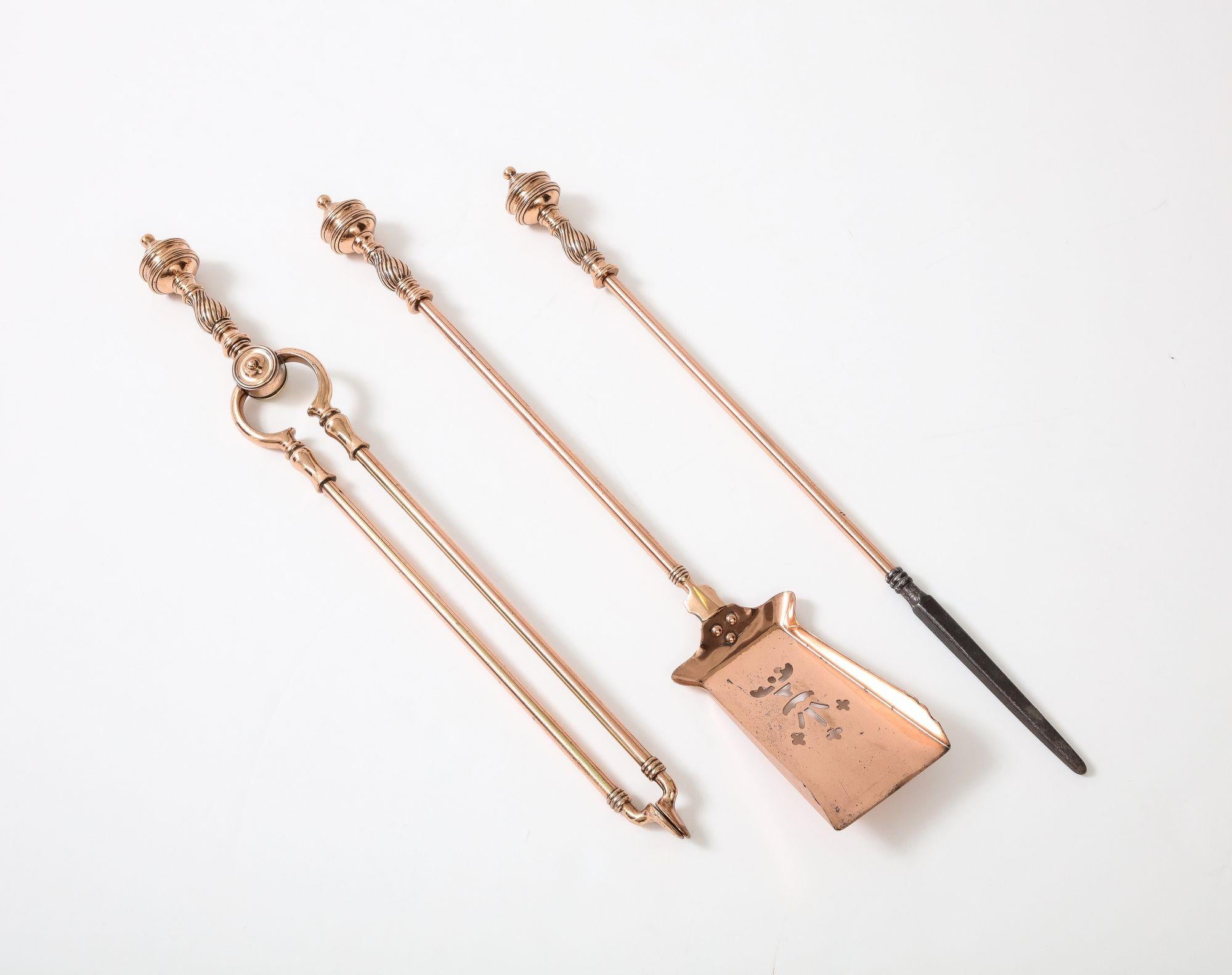 A set of three fire tools with bold turnedcopper handles and shafts comprising: a poker with forged iron tip, tongs and a flared shouldered shovel with pierce-work decoration.  England, circa 1870. 
 
AD