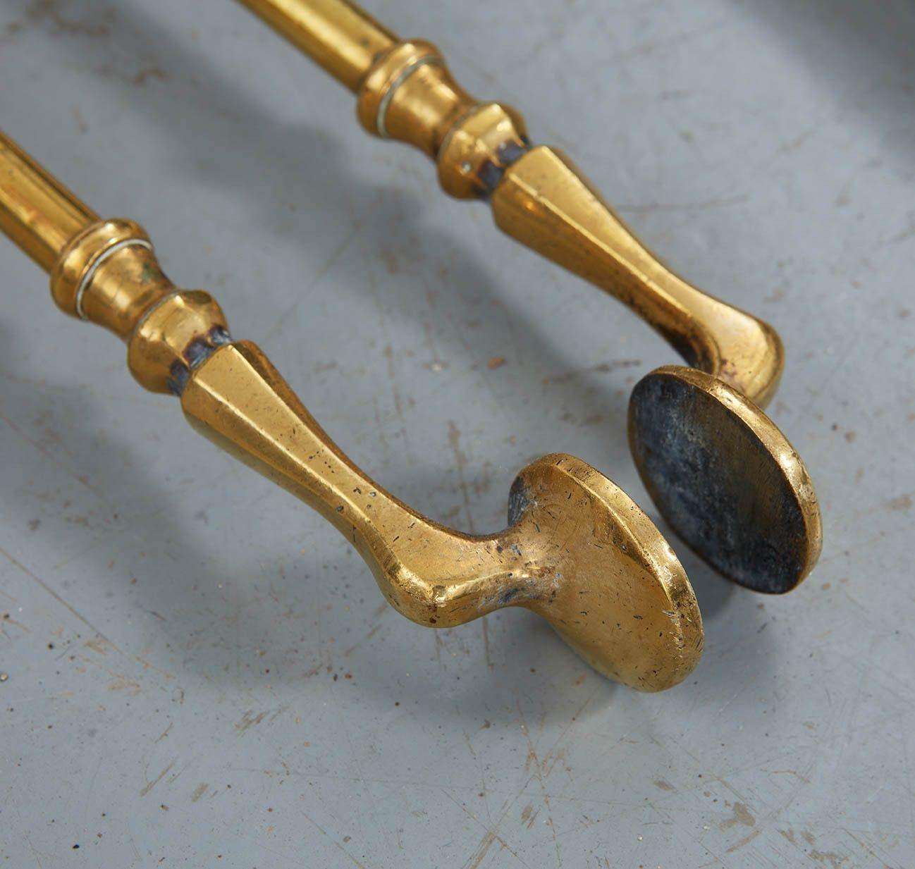 A set of three brass firetools comprising poker, tongs and shovel having flattened octagonal brass knob finials and brass shafts with ring turnings, the shovel bowl of brass with rectangular border piercework and the poker with wrought iron tip.