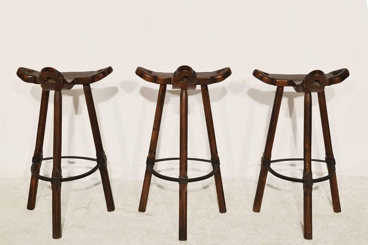 Set of three 'Brutalist' bar stools, in stained beech and metal, Spain, 1970s. A curved T-shape with three handles. The curved form makes sure the stool has a stabile seat, emphasized by the metal ring as footrest.