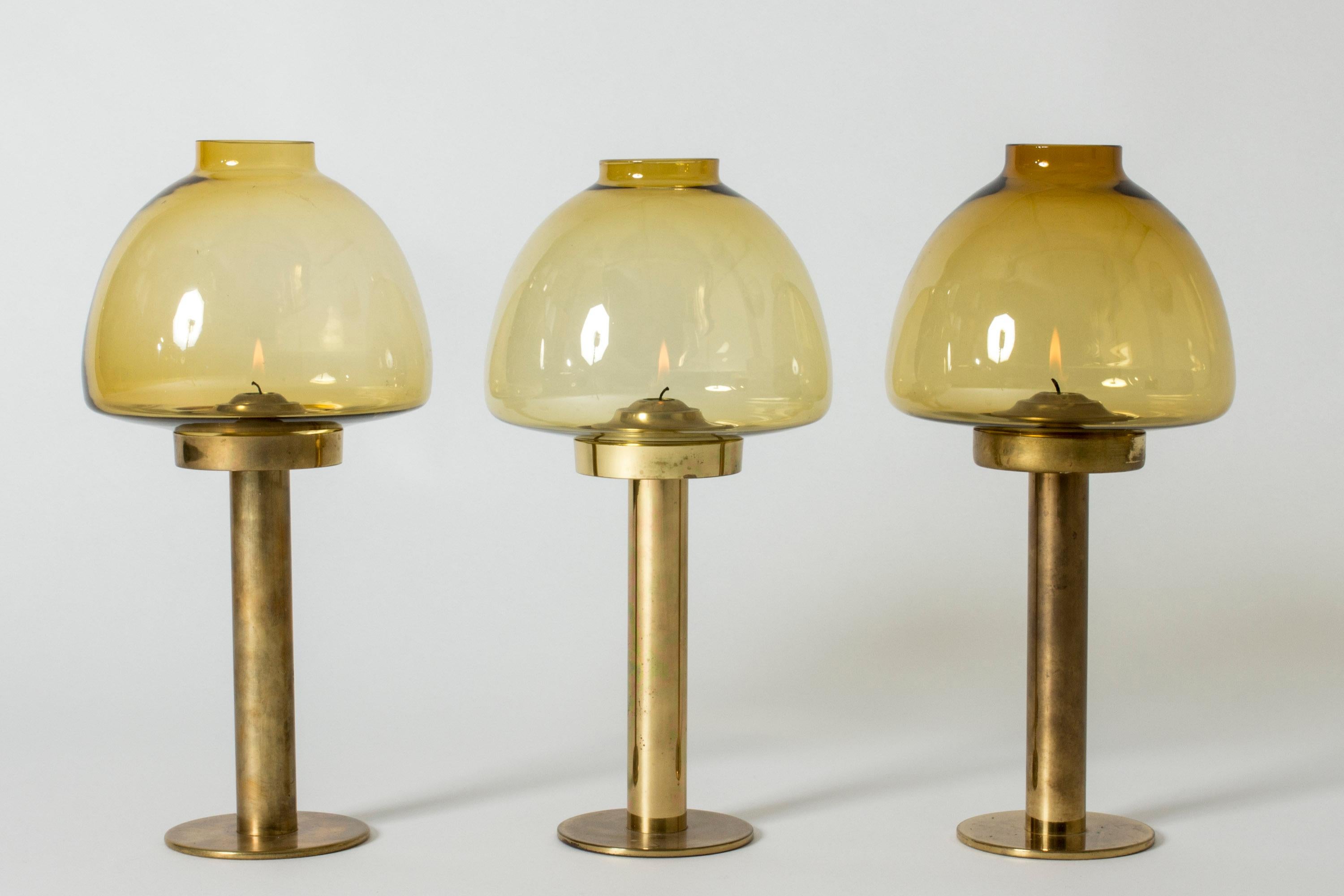 Set of three elegant candlesticks by Hans-Agne Jakobsson in an original design. Made from brass with large, smoke colored glass shades. Regular candles are placed inside the stems and springs inside keep the flames in the same position as the