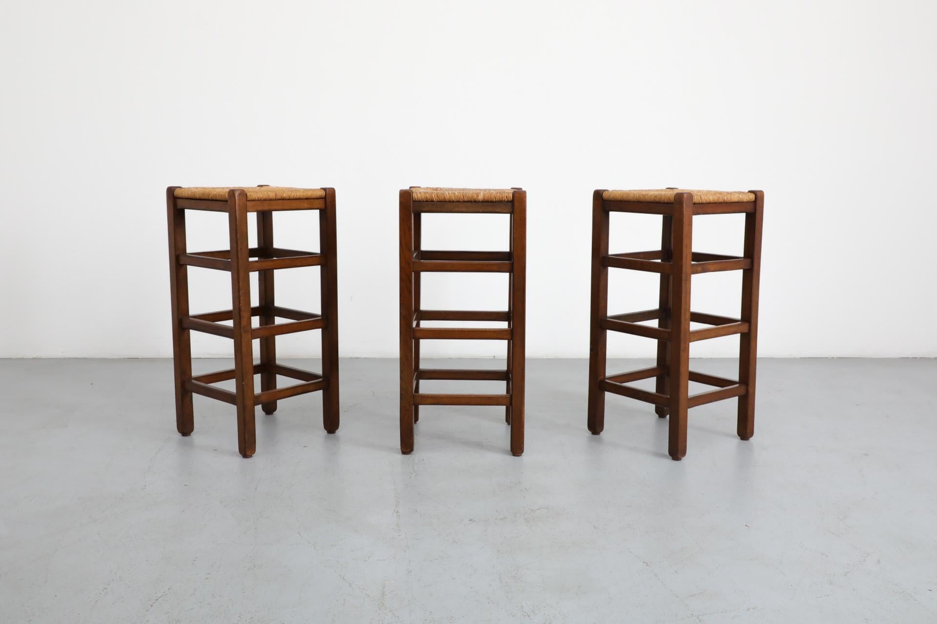Set di 3 sgabelli da bar in stile Charlotte Perriand con struttura in rovere tinto scuro e sedili in giunco intrecciato. L'altezza della seduta è di 32