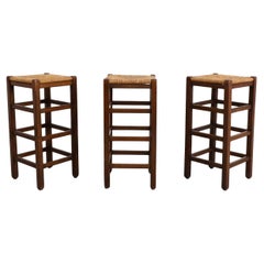 Juego de tres taburetes de bar estilo Charlotte Perriand de roble teñido oscuro y junco