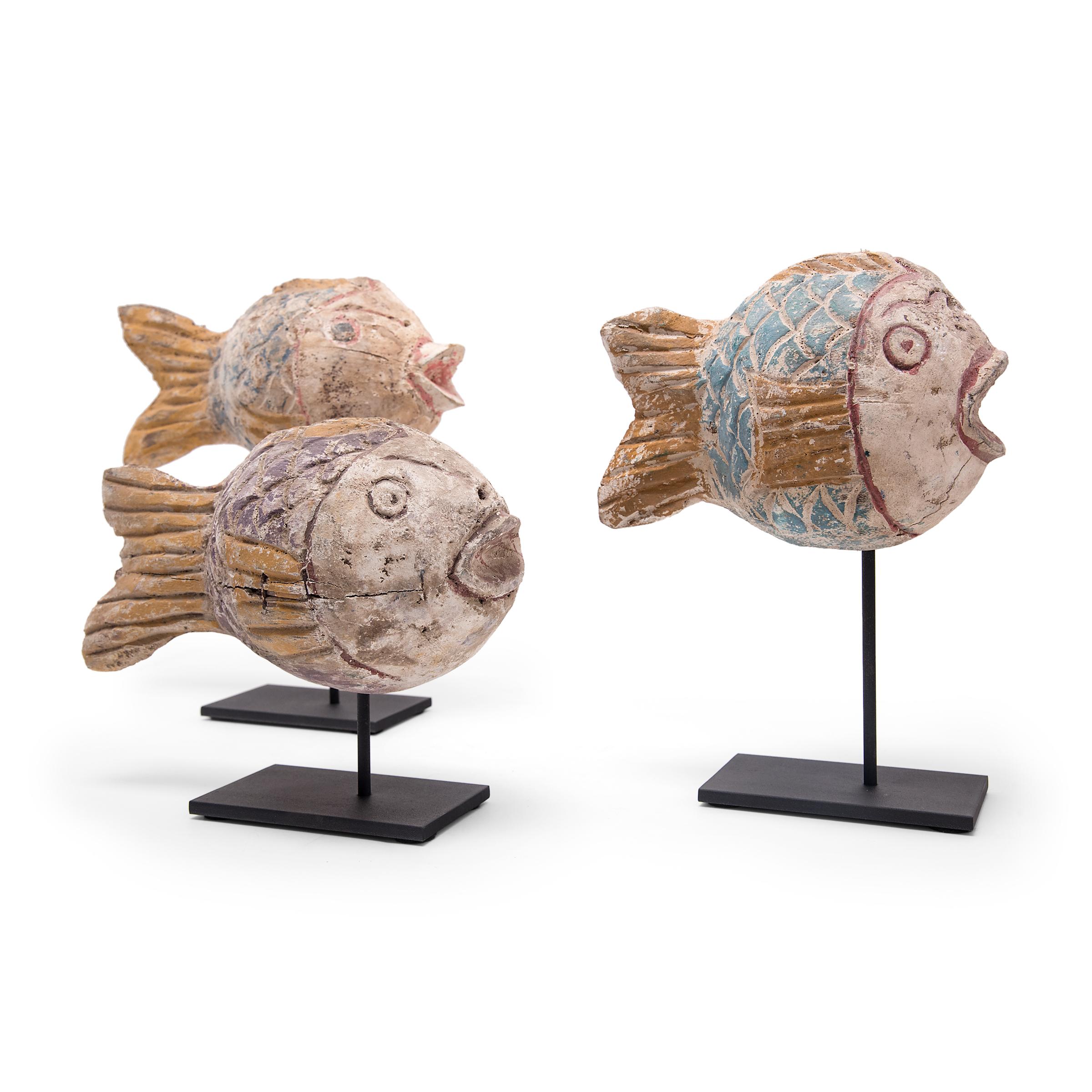 Hand-carved from reclaimed wood, these rustic koi sculptures recreate early 20th-century Chinese Folk Art designs. Each fish is carved with a squat, rounded body and painted with a colorful palette of blues, purples, and yellows. Common motifs in