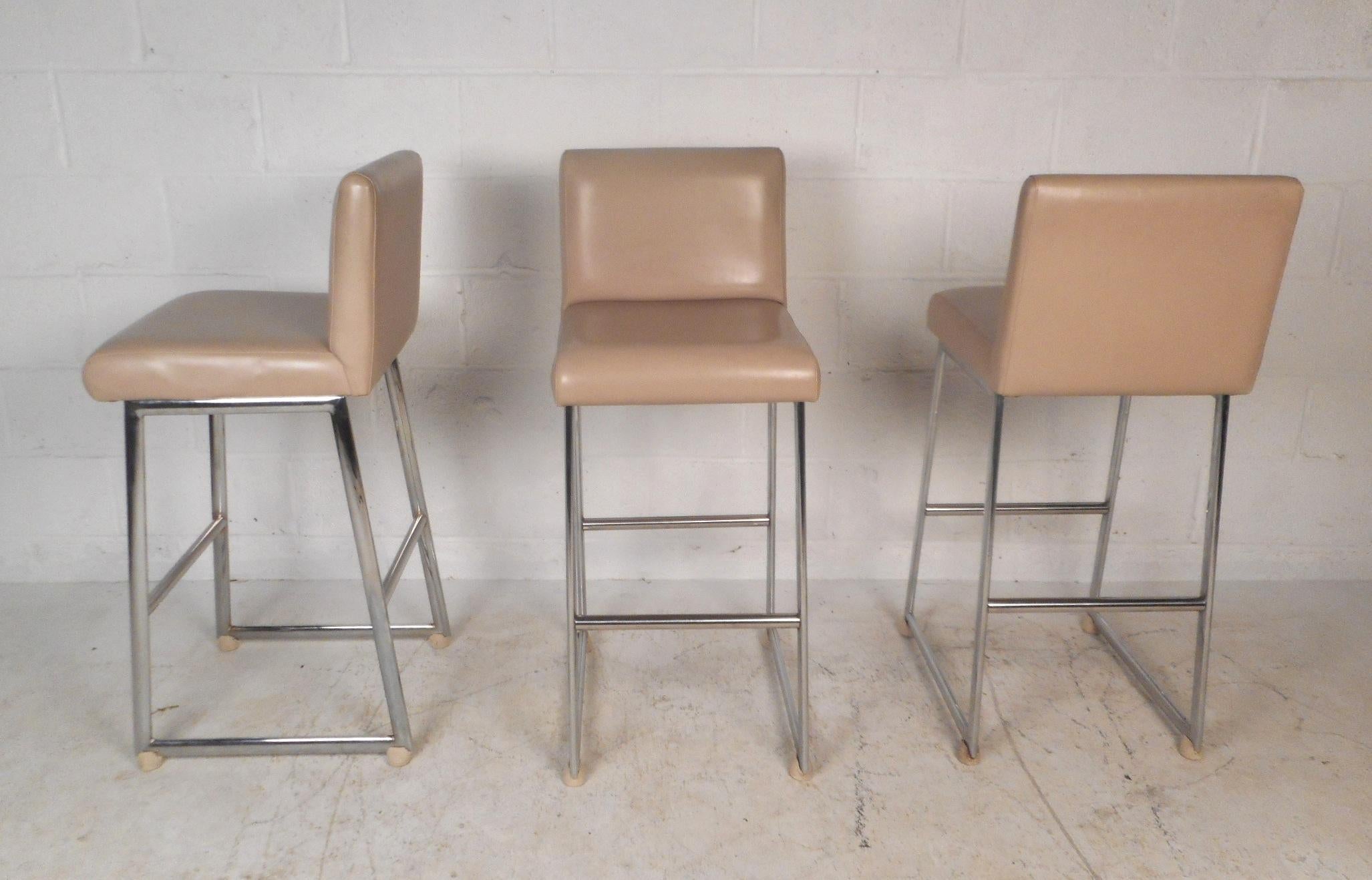 A stunning set of three vintage modern bar stools with chrome frames and thick padded seating covered in beige vinyl. The unique slipper design offers a comfortable and stylish place to sit. This beautiful mid-century set of bar stools make the