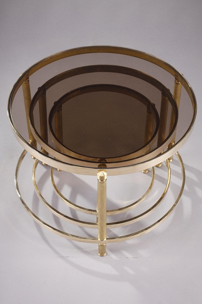 Three nesting coffee tables in bronze, brass and smoked glass from the 1970s, in the taste of the Houses of Ramsay and Jansen. The structure of each piece is composed of three fluted barrel legs, connected by a semi-circle at the bottom. The bronze