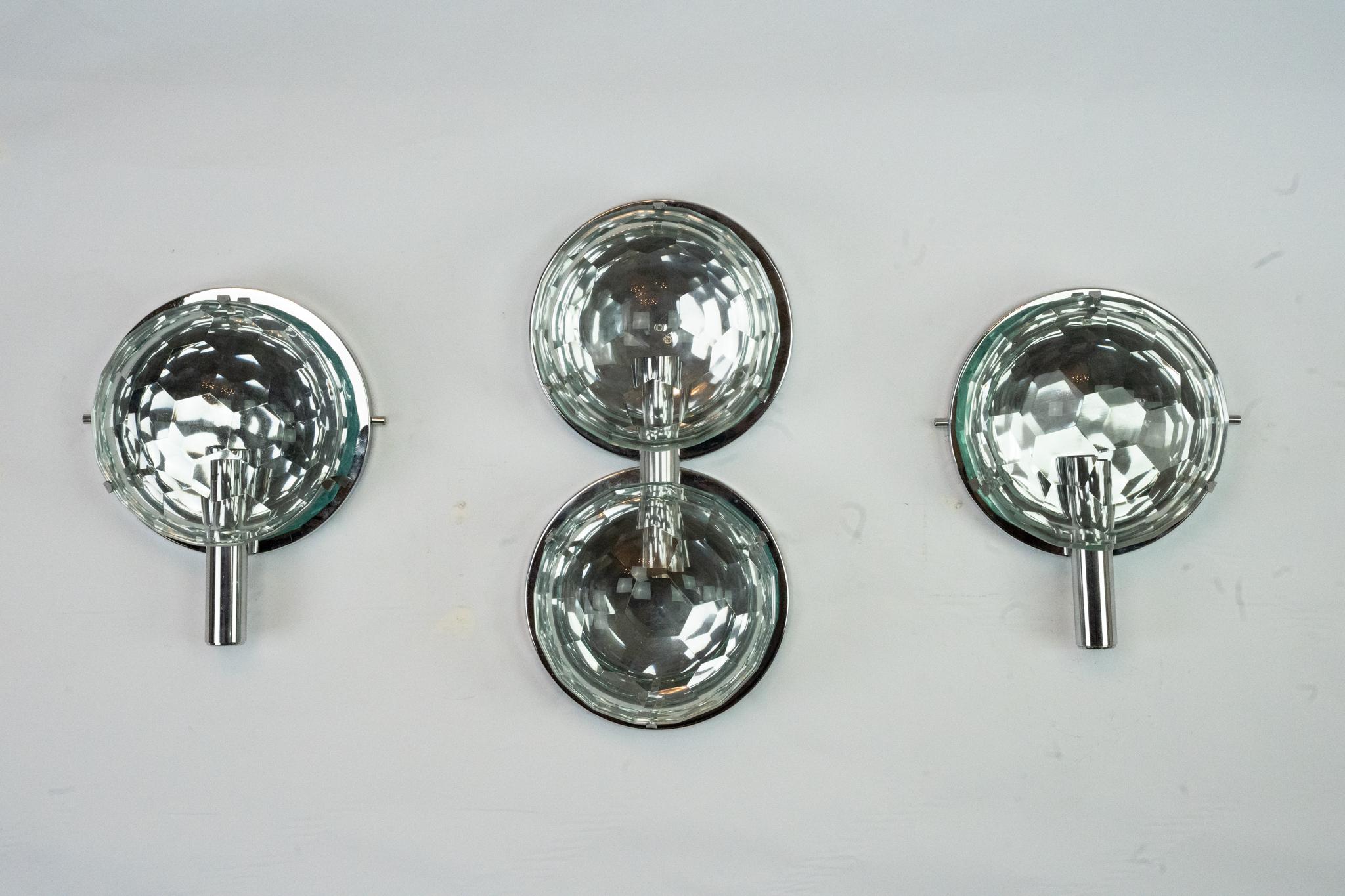 Este conjunto incluye tres apliques de pared italianos de mediados de siglo diseñados por Cristal Arte en la década de 1970. La pieza central presenta una configuración de doble luz con cúpulas de cristal tallado facetado montadas sobre una