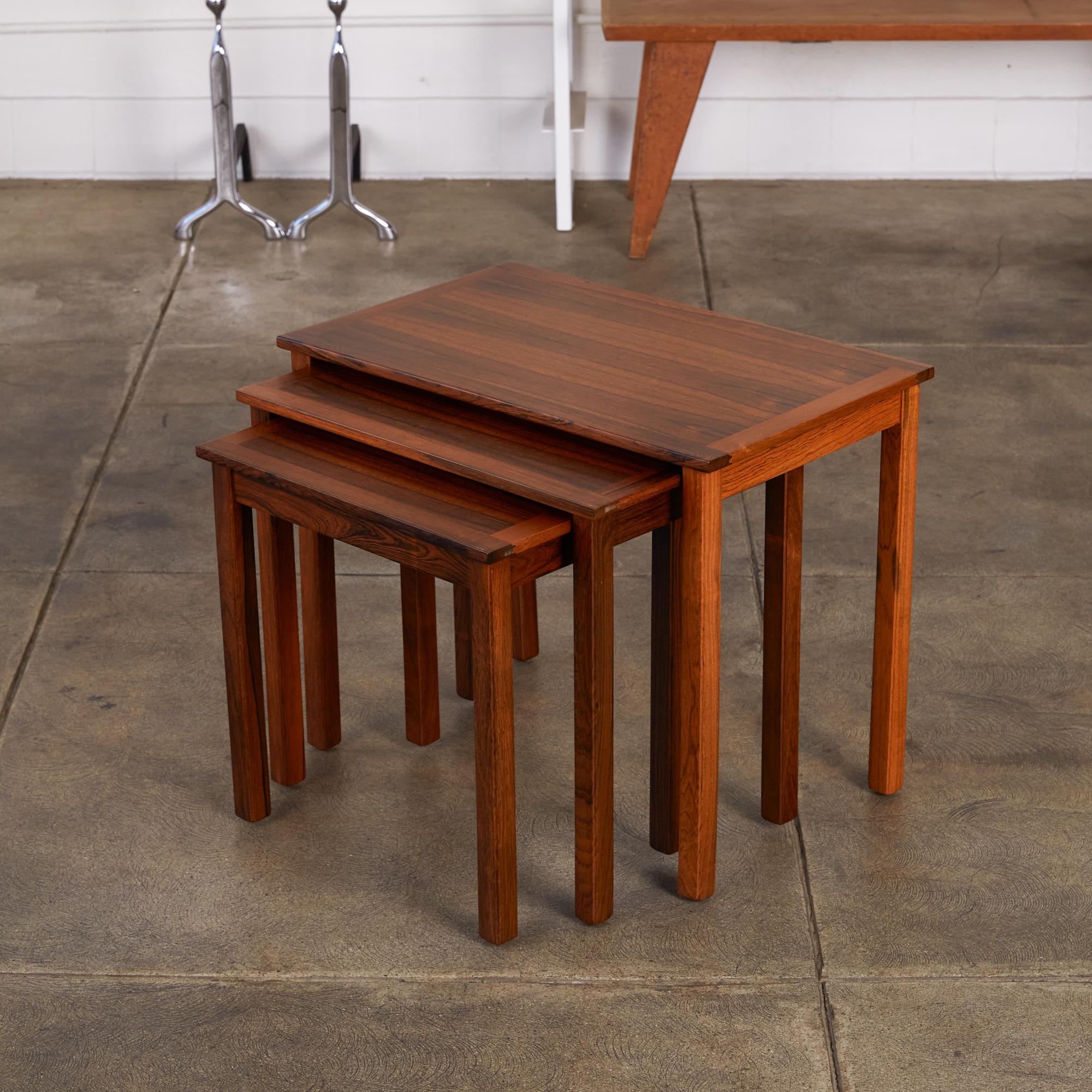 A set of Danish nesting tables in rosewood. Table design has square, slightly recessed legs, and a tabletop beautifully edged with contrasting wood grain. A set of concealed, parallel runners allows each smaller table to slide easily under the
