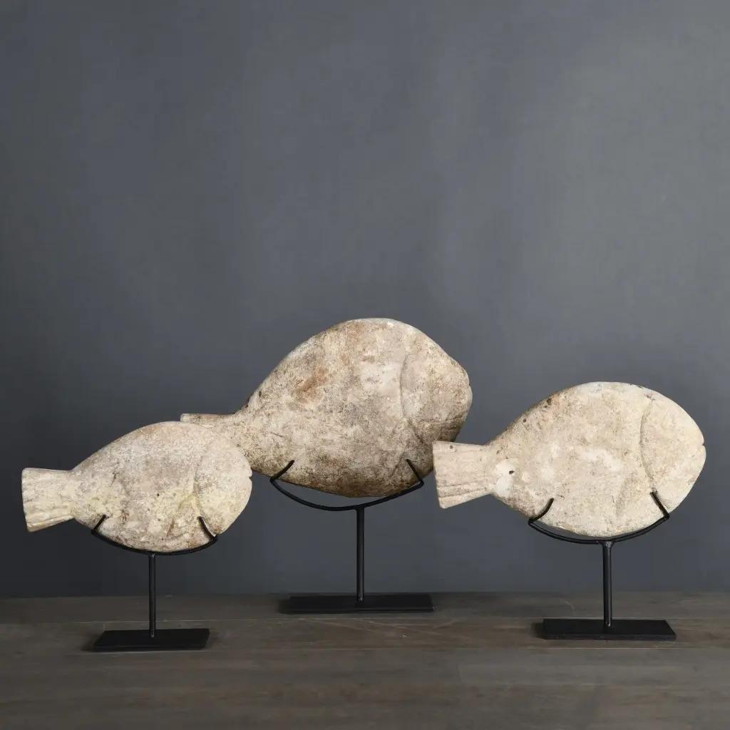This set of three decorative stone fish is a unique handcrafted piece from Indonesia, where fish are revered as divine symbols of luck and gratitude. Weathered with time, the sculptures display a natural patina that enhances the raw texture of the