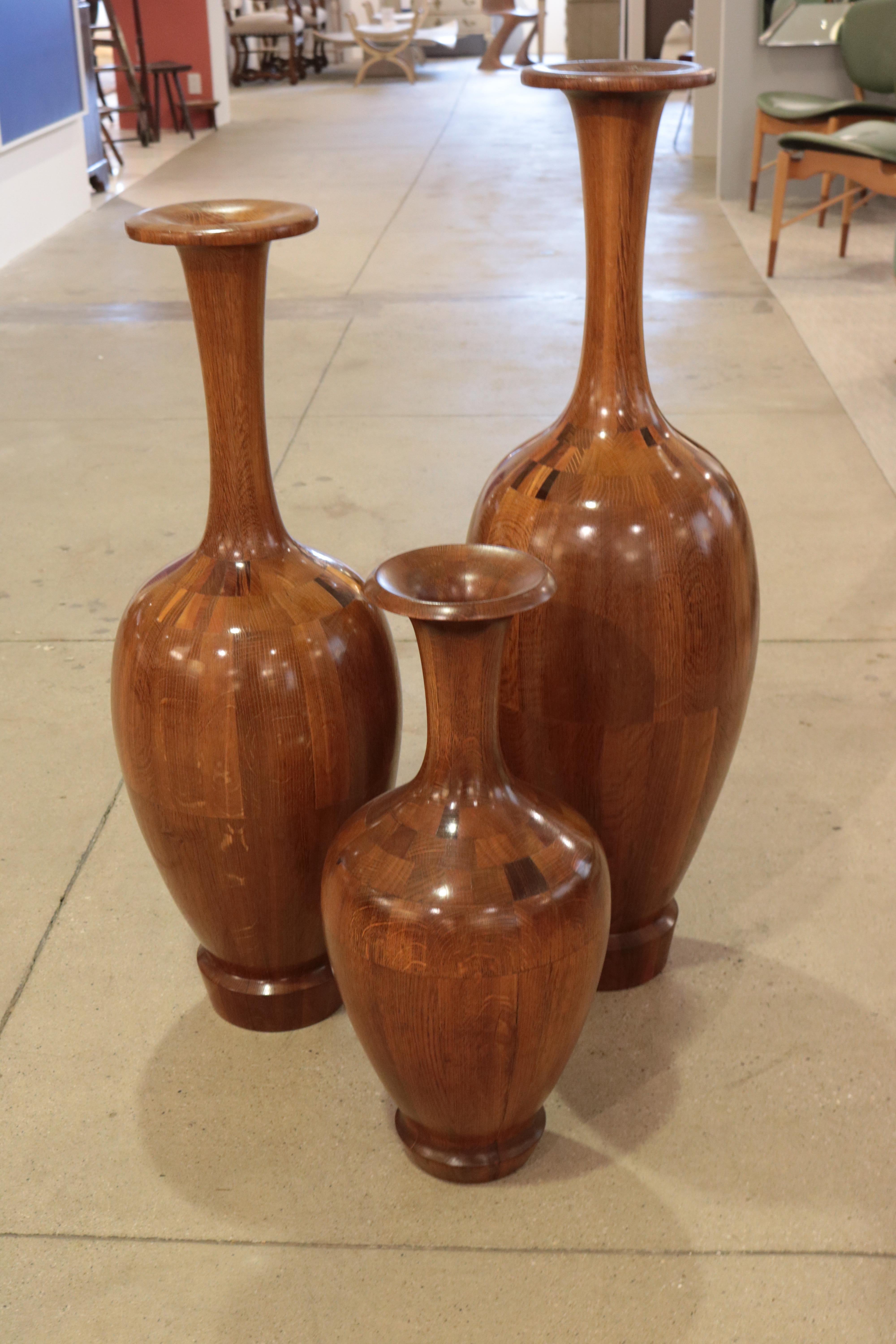 Set of three large decorative wood vases by De Coene Frères. Various woods with decorative marquetry details at the neck of each.

1) H:38 D:12
 2) H34: D:11 
3) H:23 1/2 D:10 1/2 Inches.