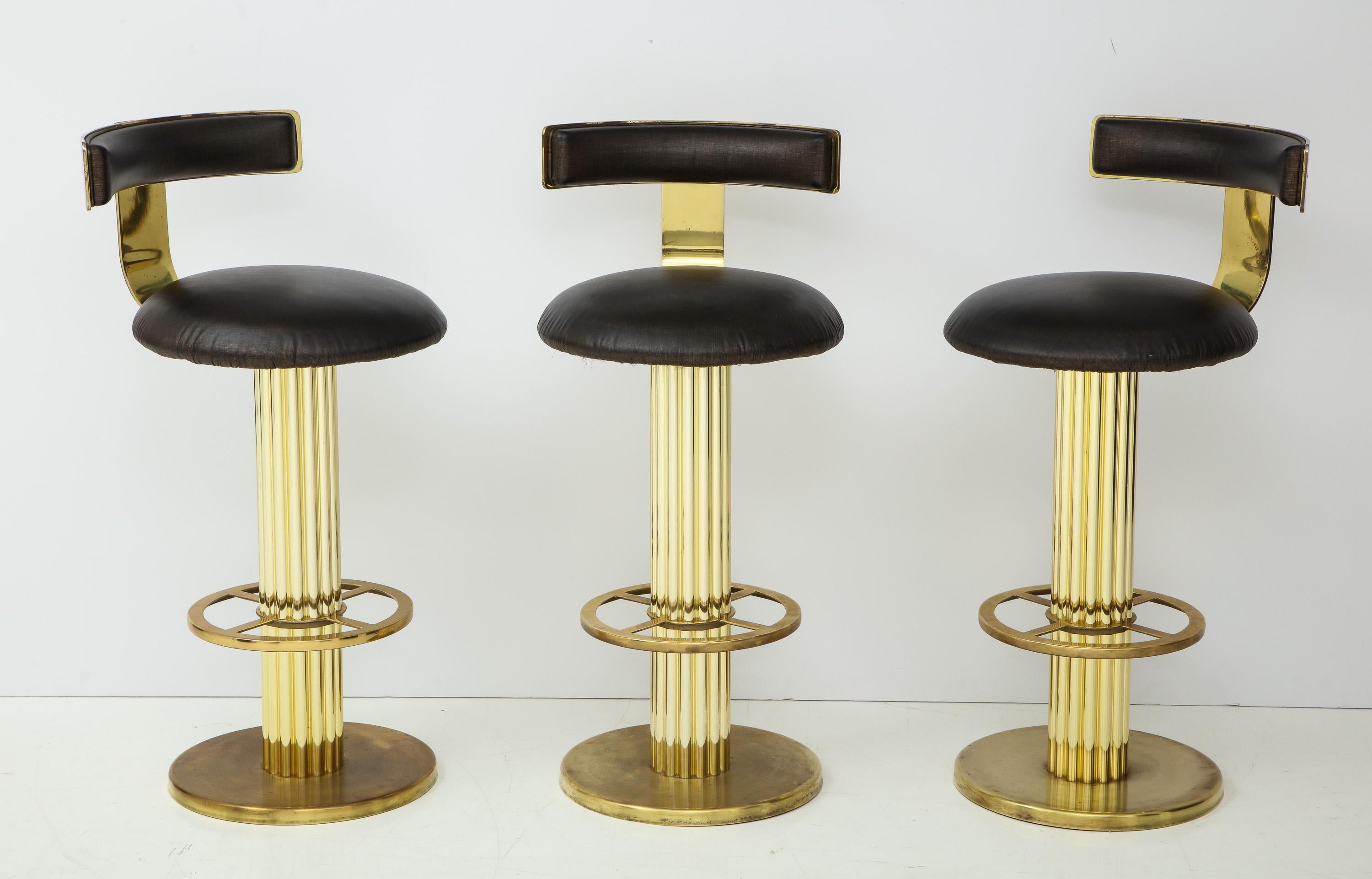 Set of three swivel barstools in uncommon brass finish, produced by Designs for Leisure, circa 1980s. Well-made and heavy, with fluted column supports that include footrests. Price is for the set of three.