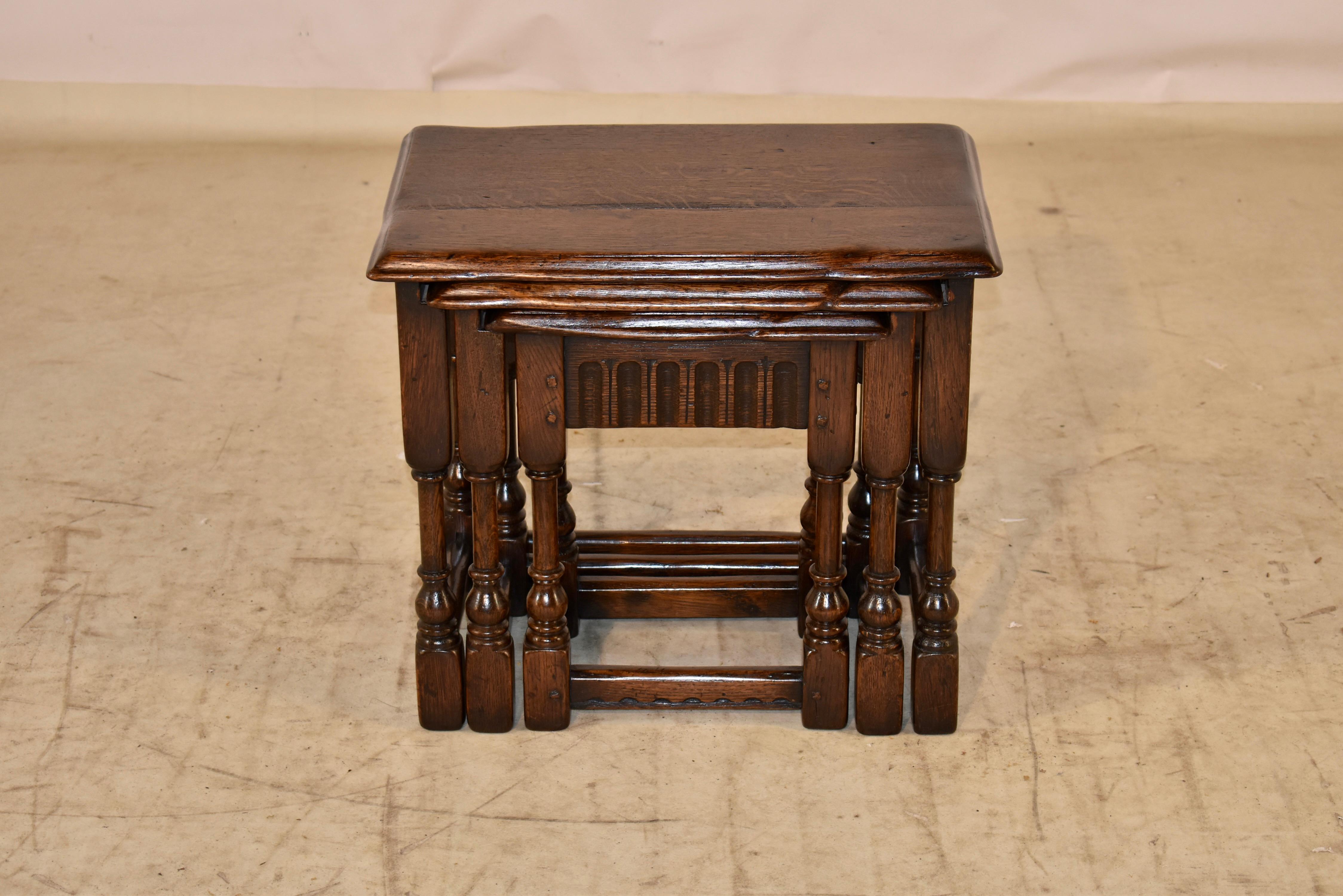 Set of three oak nesting side tables from England.  The tops have gorgeous patina and graining, and have eased beveled edges.  The aprons have hand carved decoration and all of the tables are supported on hand turned legs, joined by simple