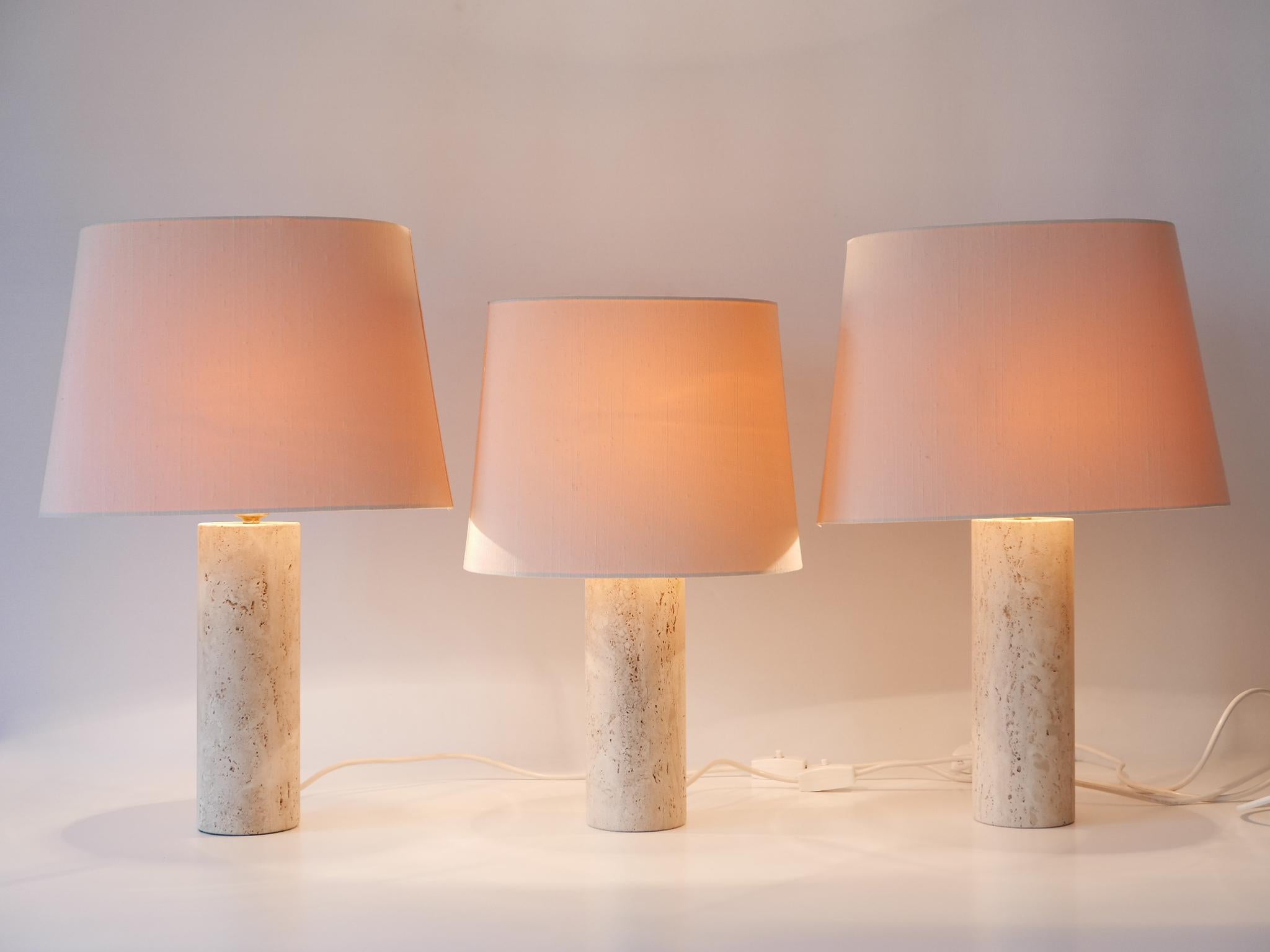Set of three elegant Mid-Century Modern table lamps or bedside table lamps with travertine bases and fabric shades in silk. Designed and manufactured in Italy, 1960s.

Executed in travertine and silk shades, each table lamp comes with 1 x E27 / E26