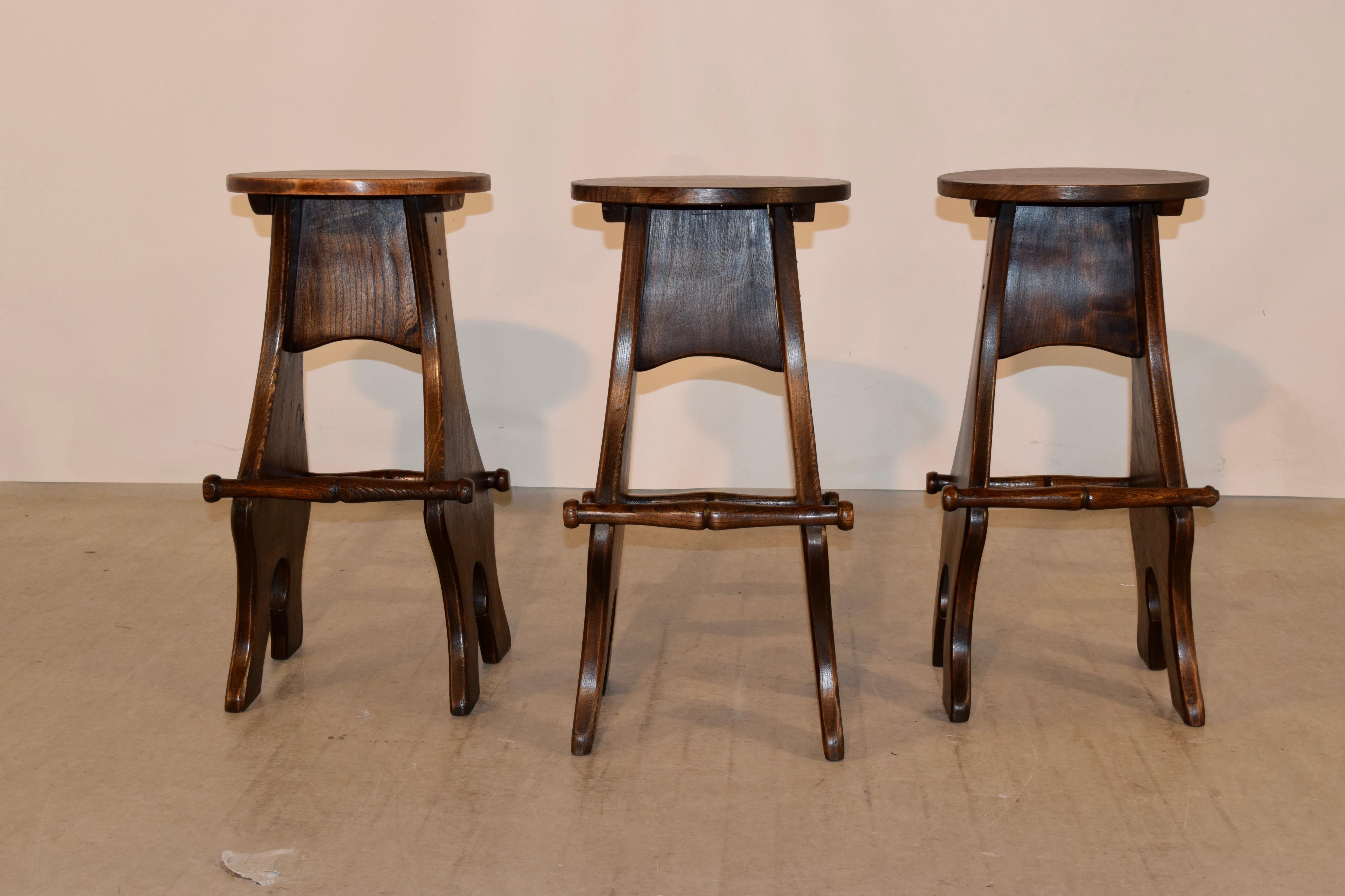 Set of three English barstools, made from oak and elm. The seats are made from oak and are resting on unusual bases made from elm with unique shape and two different length of hand-turned footrest - one side is for longer legs and the other side for