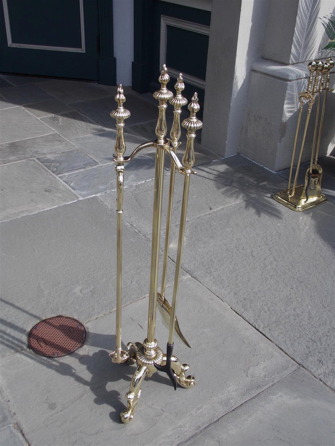 Set of three English brass fire tools on stand with flame finials, bulbous melon handles, circular centered melon column, and resting on three decorative scrolled engraved feet. Set consist of shovel, tong, and poker, Mid-19th century.