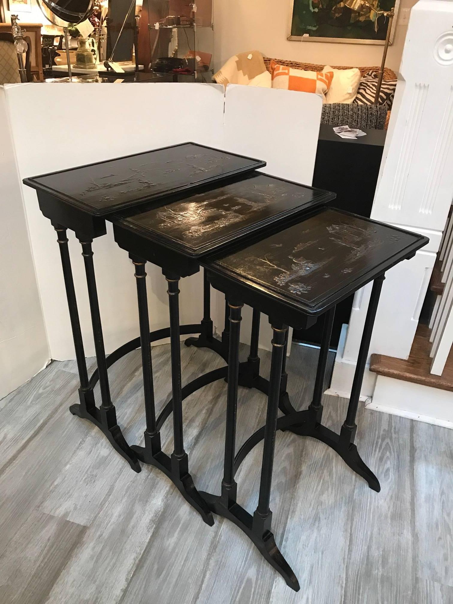 Three Classic English Regency style chinoiserie nesting tables. The largest with two smaller tables that fit neatly into one another. The finish is a japanned black background with gold scenes of Asian inspires people and landscapes, early 20th