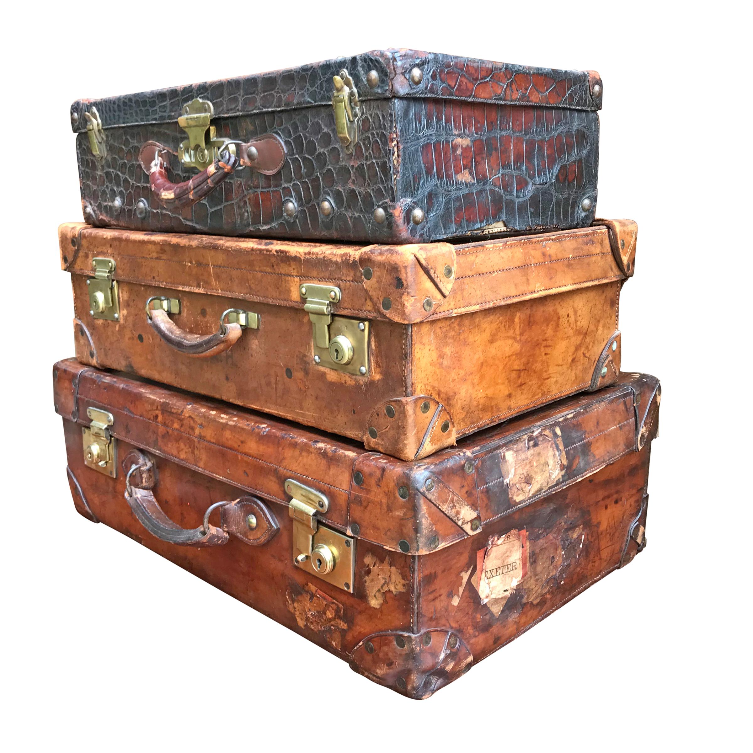 A fantastic set of three early 20th century English Edwardian period leather suitcases including two thick belting leather cases with polished brass hardware and the third case being made from crocodile, also with brass hardware. The largest case