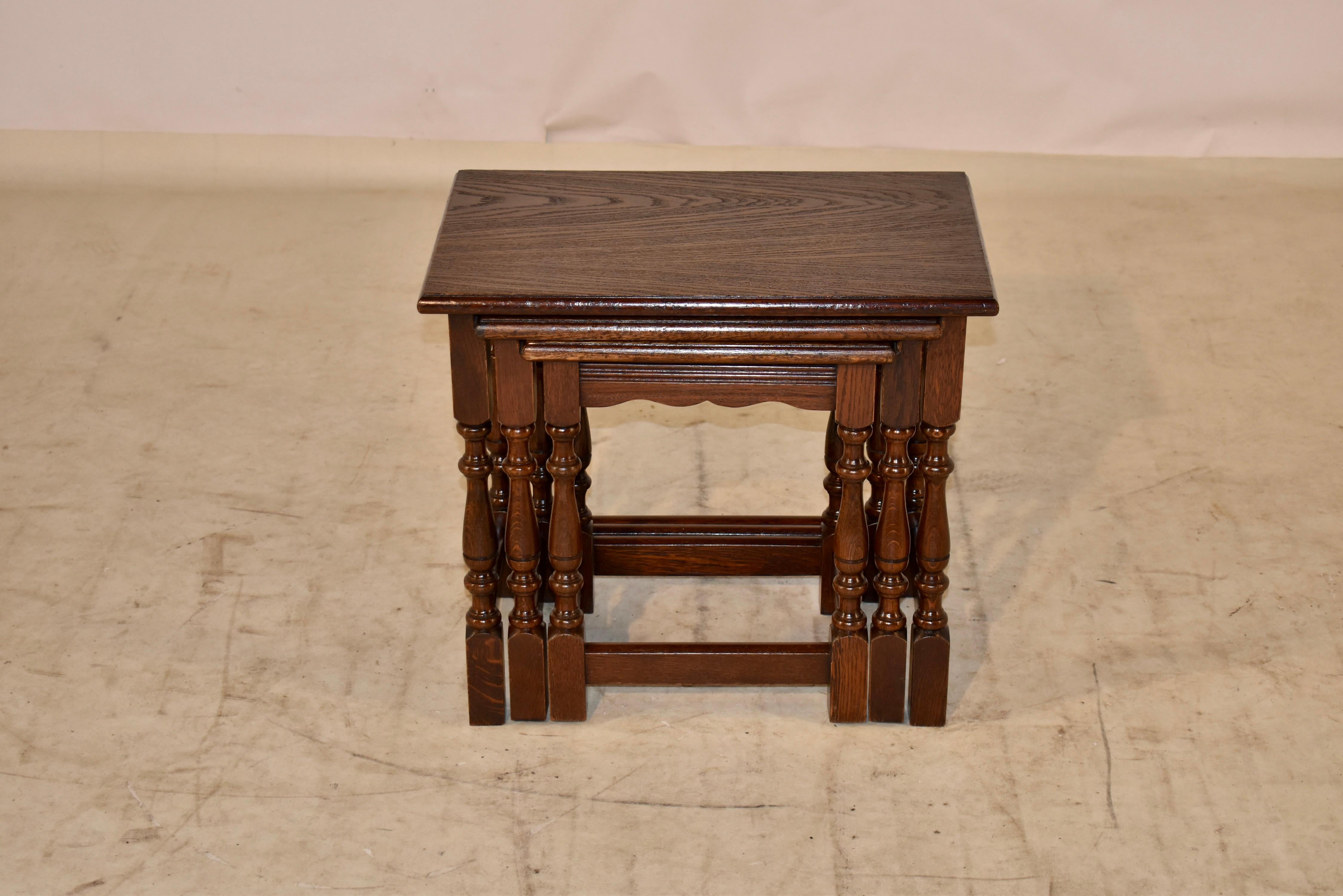 Set of three nesting oak side tables from England. Tops of the tables have beveled edges, following down to simple aprons with channeled decoration and supported on hand turned legs, joined by simple stretchers. The small table measures 13.13 w x