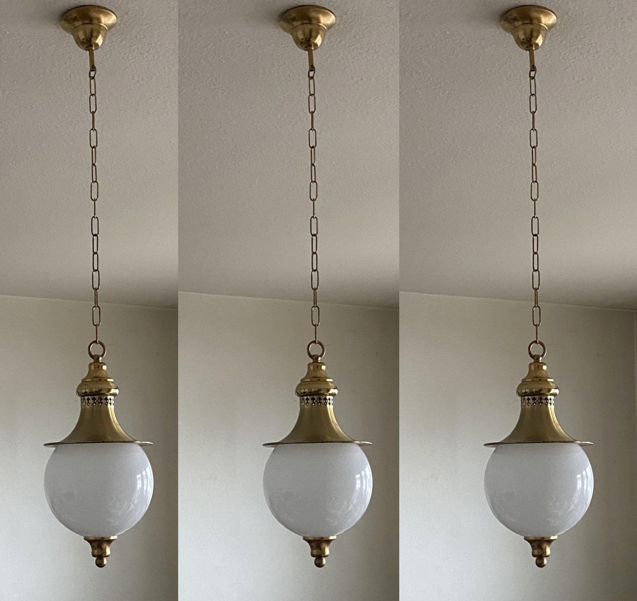 A beautiful and rare set of three hand-blown opaline glass ceiling pendants with brass gallery, England circa 1930.
Most unusual opaline glass ball with finial underneath brass shade with pierced details for light projection.
Brass with wear