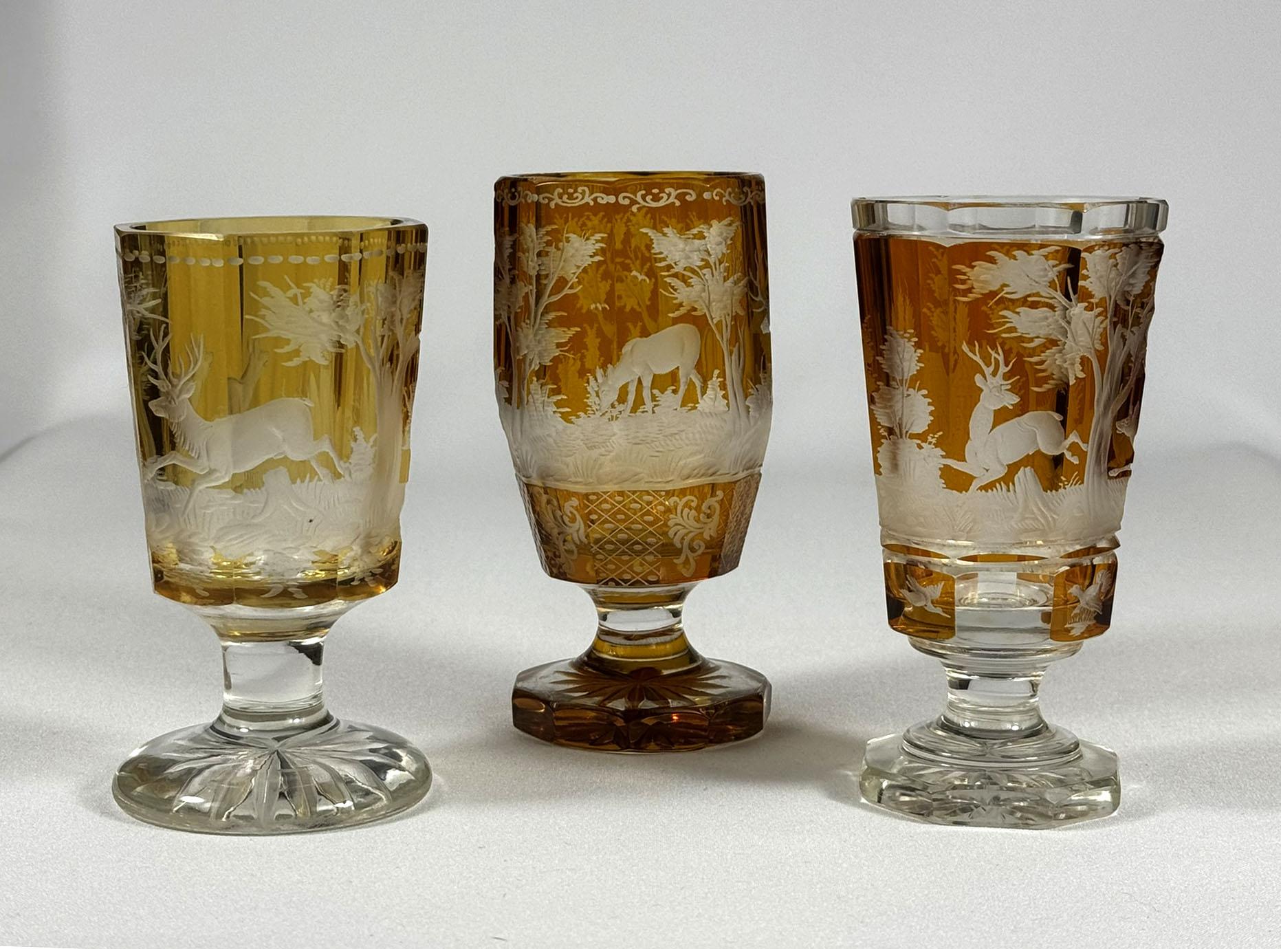 Set of three cut and engraved goblets from the first half of the 20th century. Goblets are cut from clear glass and amber lazure. The engraving is in a hunting style, a doe and a deer, popular topic in the 19th-20th centuries. Goblets are undamaged.