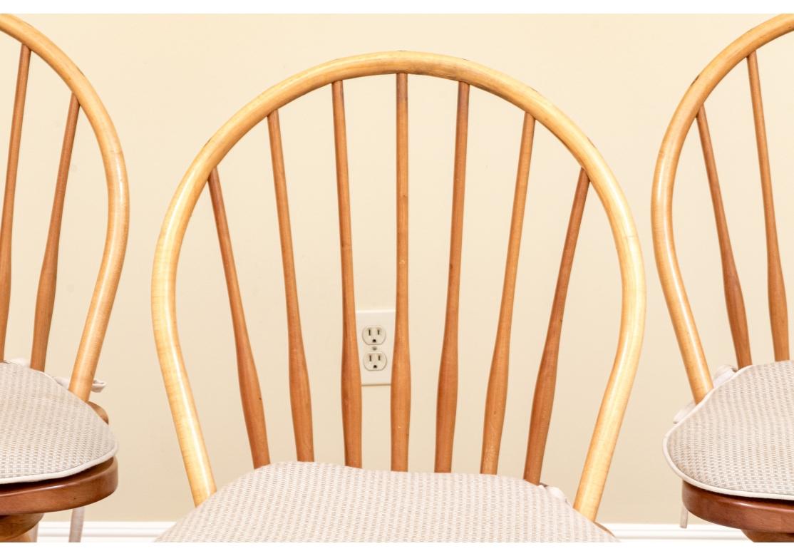 A set of 3 very well made solid cherry and beech wood Windsor style full swivel counter stools with pegged construction, turned legs and stretcher and a saddle seat. The tapering back spindles with visible contrasting wedged tips that add interest